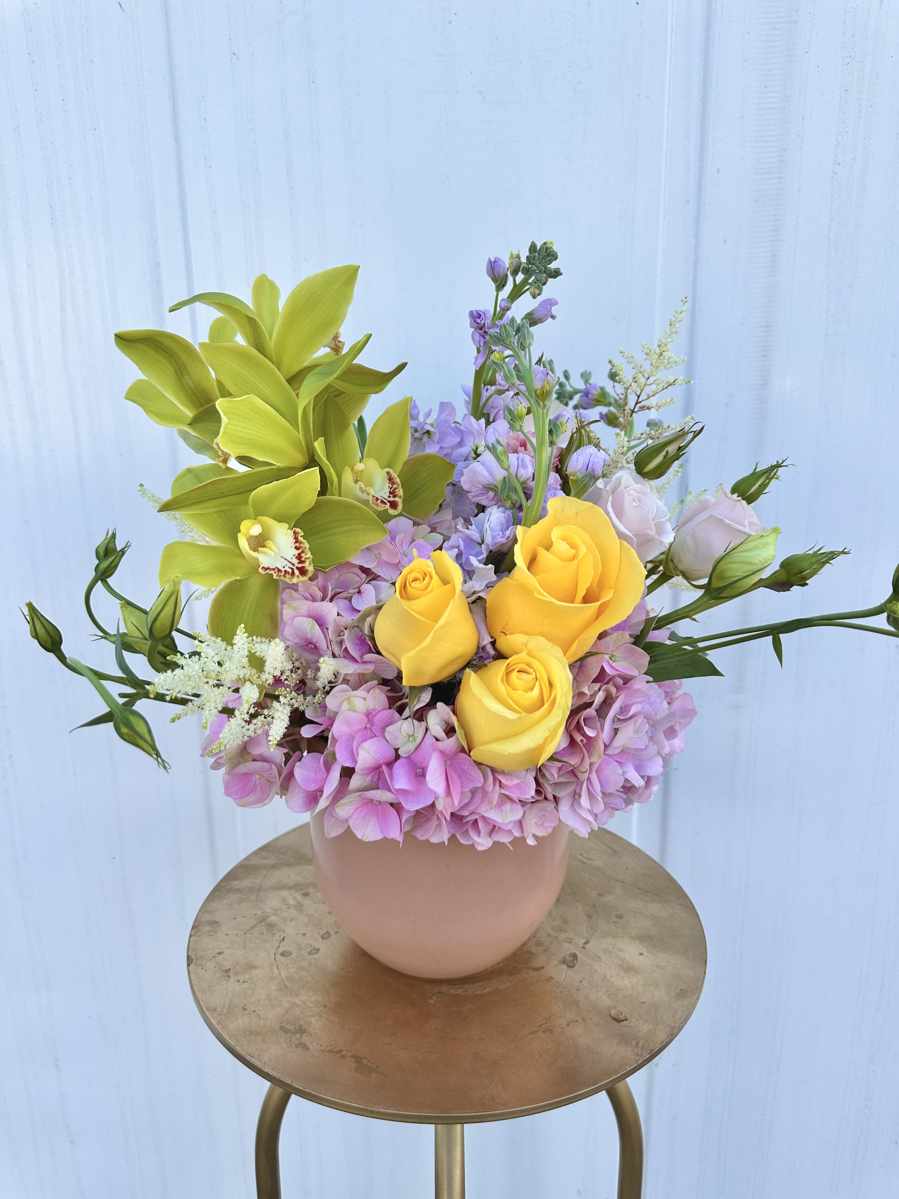 Bouquet of yellow roses, green orchids, and pink hydrangeas in a blush vase