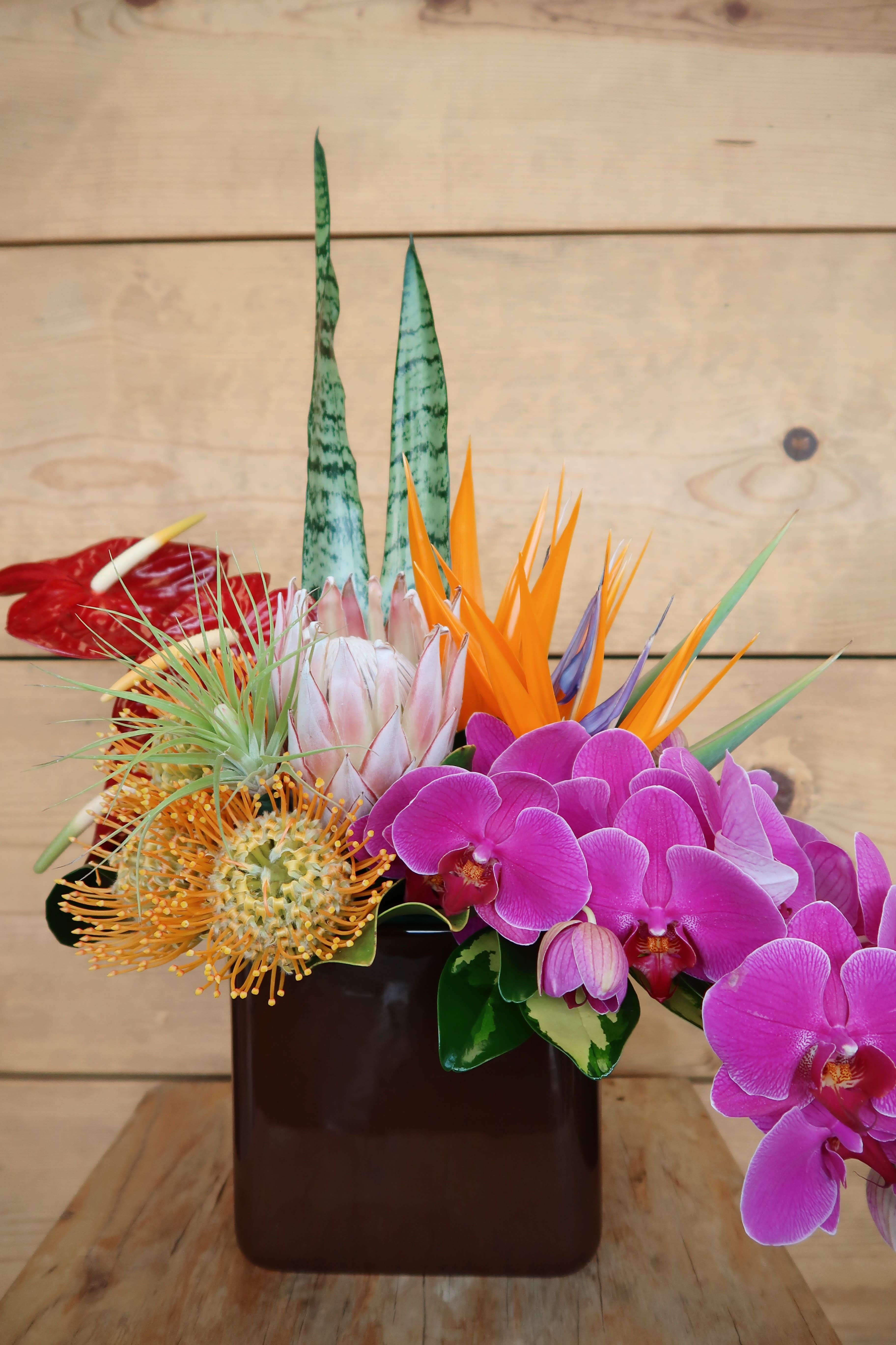 Cafe Tropical - An assortment of tropical blooms in a brown ceramic vase, perfect to brighten up any space for summer.