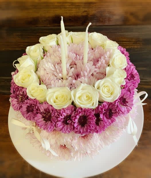 Round floral cake with white roses, pink daisies, and two candles