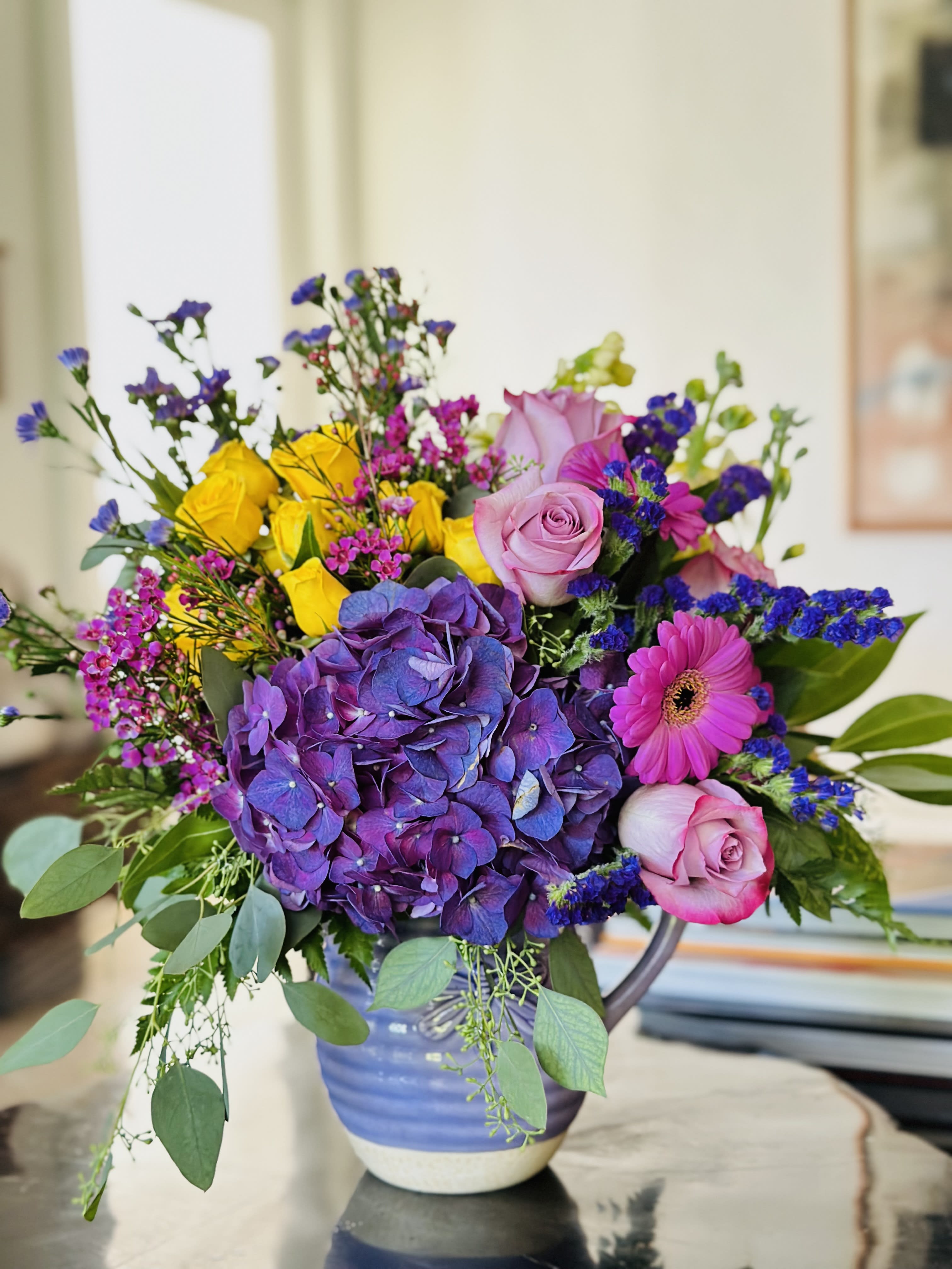 Colorful bouquet with purple hydrangea, pink roses, yellow roses, and a pink gerbera daisy in a vase