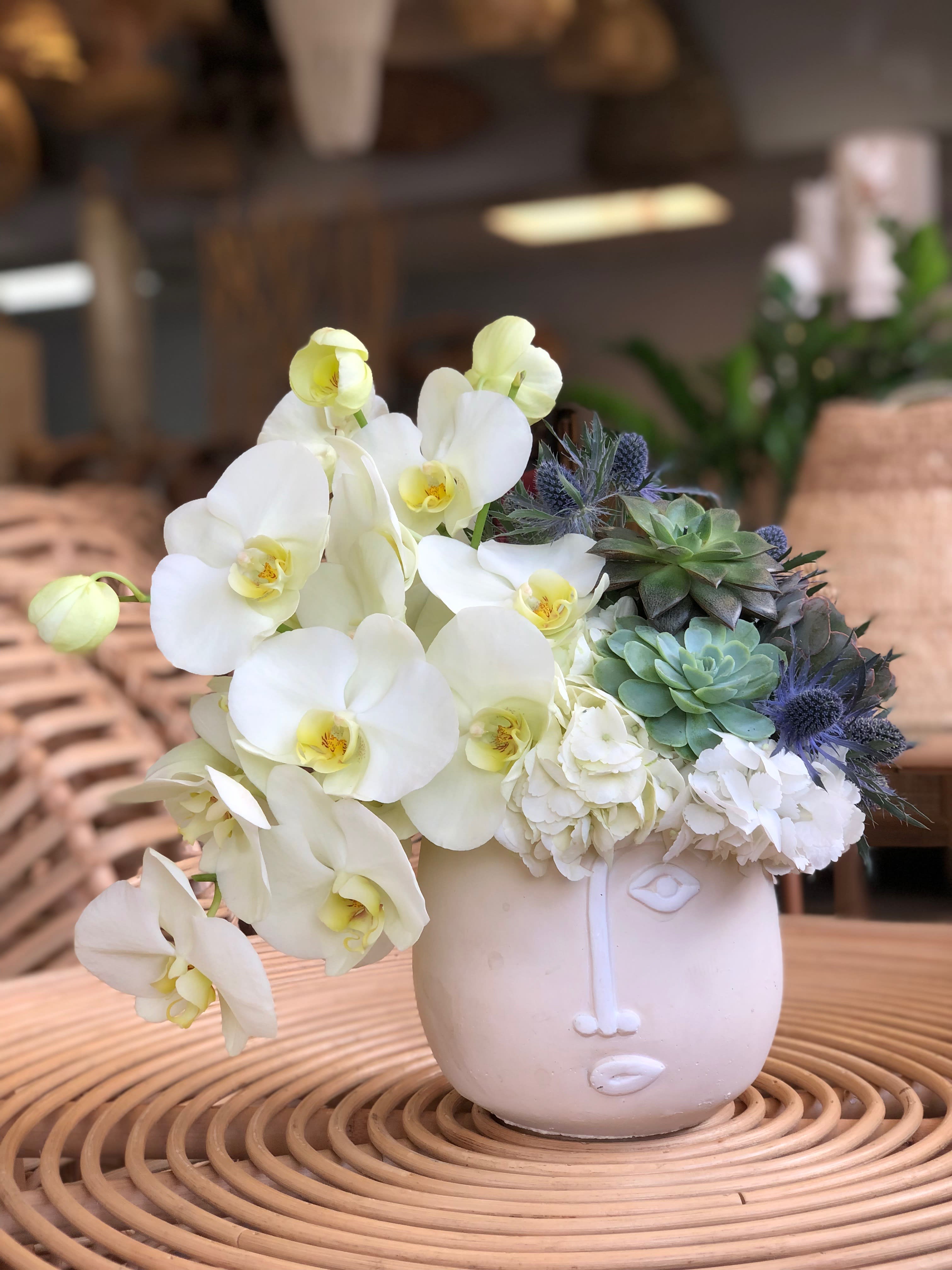 White orchids and succulents arranged in a pale ceramic face vase