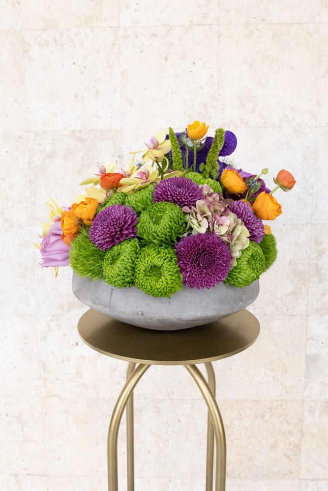 Colorful flower arrangement in a gray bowl vase on a gold stand