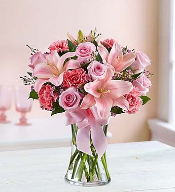 Pink roses and lilies arranged in a clear glass vase with a ribbon