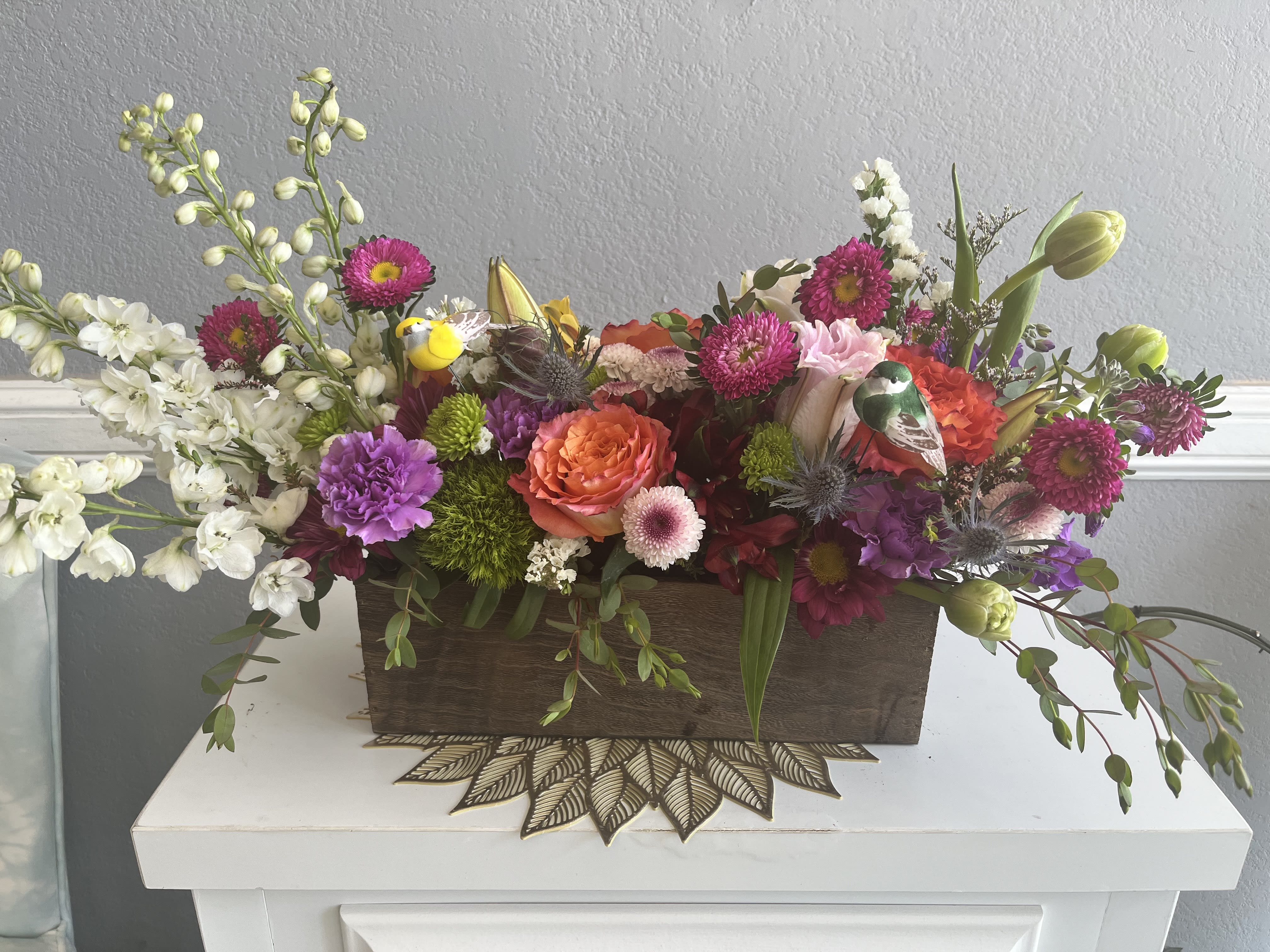 Mixed floral arrangement in a wooden box with pink, orange, white, and purple blooms