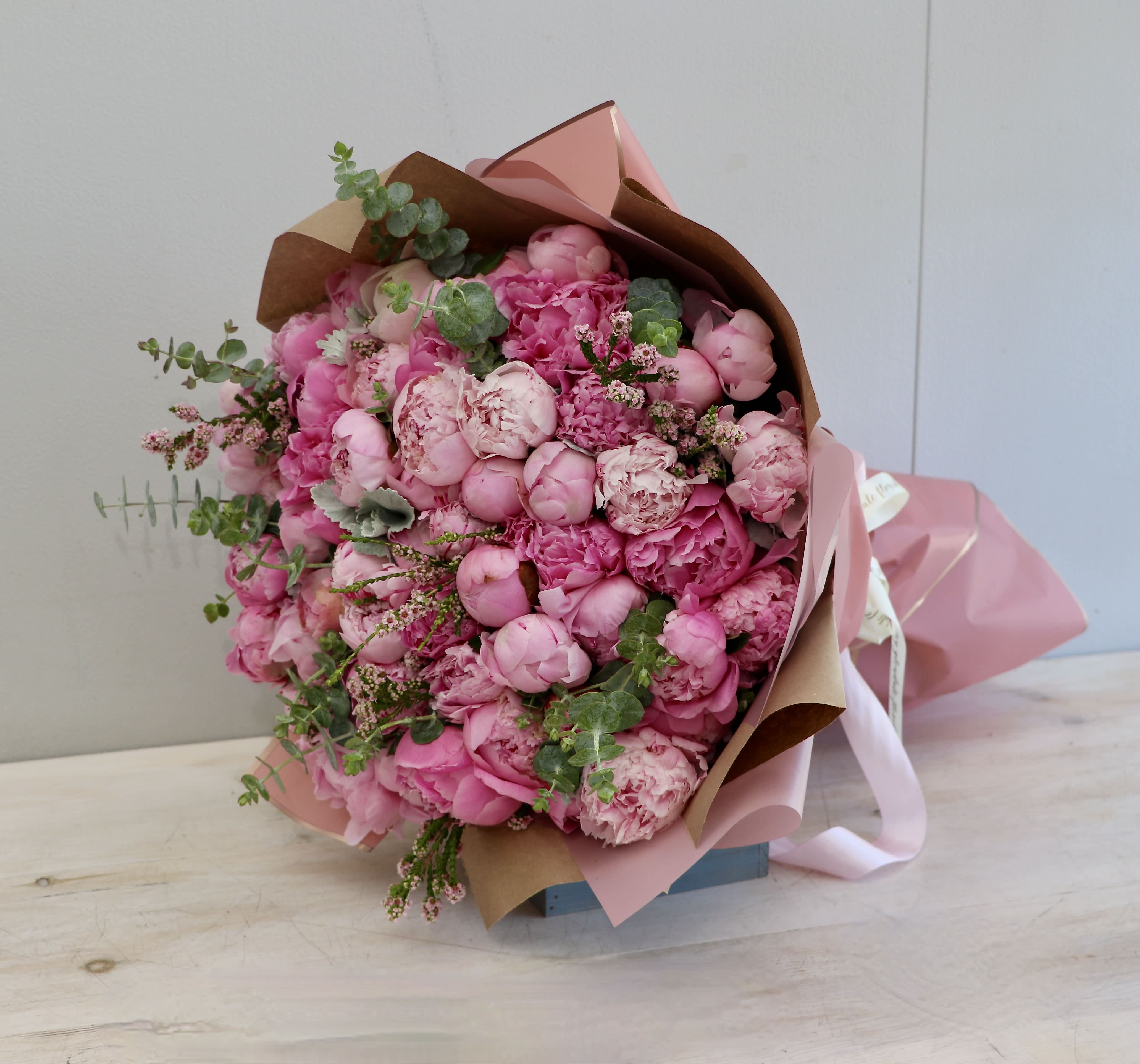 Large bouquet of pink peonies wrapped in pink and kraft paper with ribbon accents
