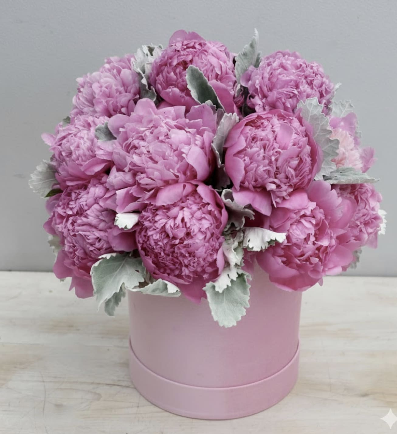 Round pink hatbox arrangement of bright pink peonies with soft silvery foliage