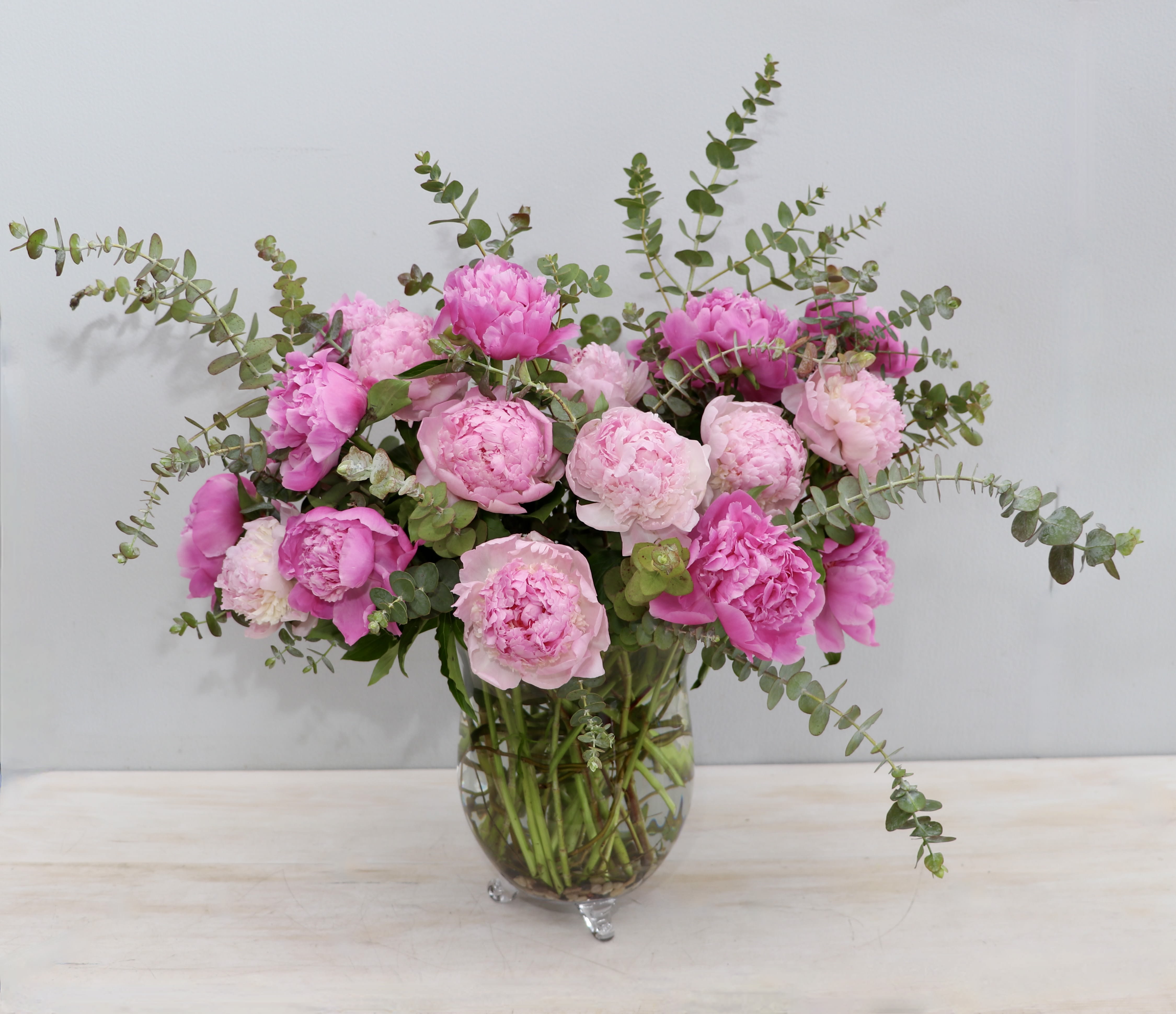Large arrangement of pink peonies with eucalyptus in a clear glass vase