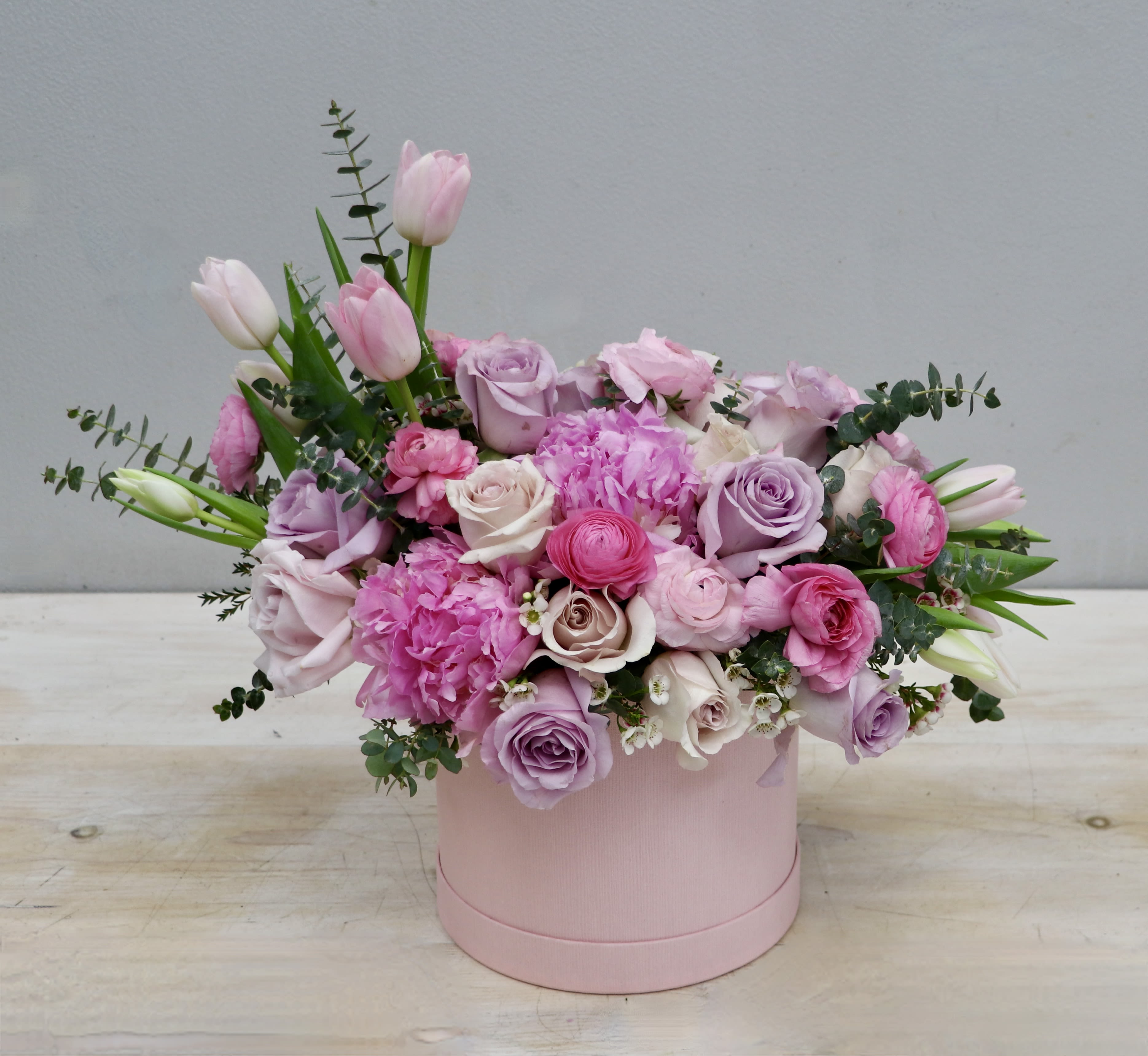 Pink and lavender roses, tulips, and peonies arranged in a round pink hat box