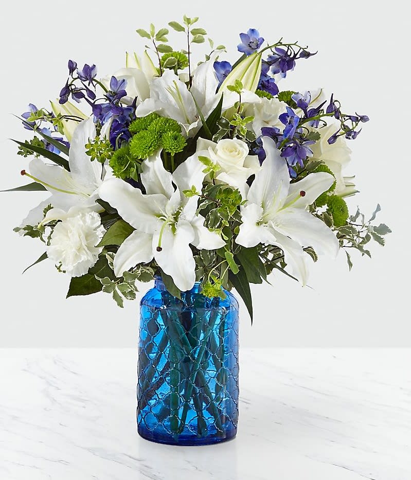 White lilies and blue flowers arranged in a blue glass vase