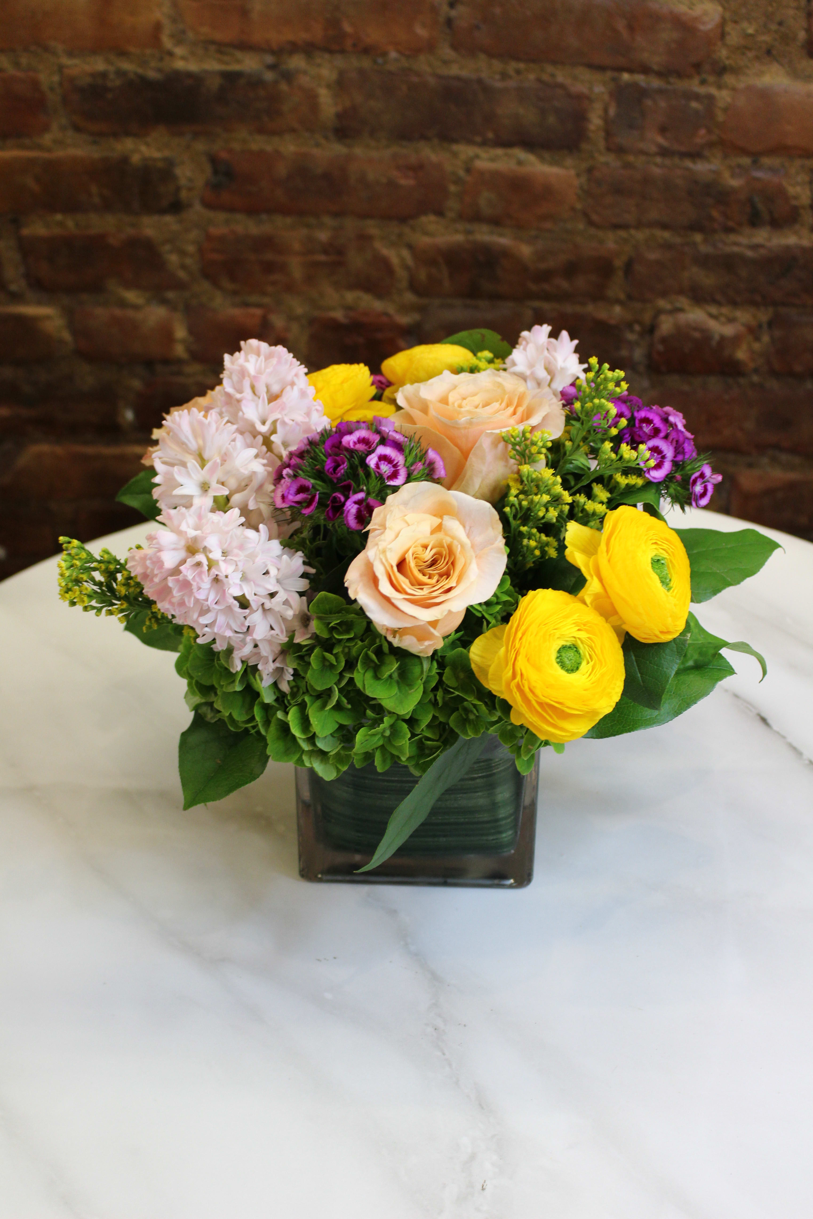 Mixed bouquet in a square glass vase with peach roses and yellow ranunculus