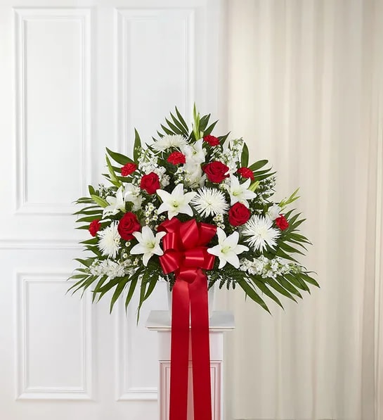 Standing floral spray with red roses, white lilies, and a red ribbon