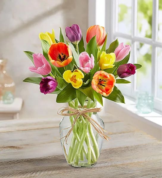 Timeless Tulips - Cheerful tulips are nature’s way of saying, Spring is here! Our timeless bouquet is filled with these feel-good blooms in a bunch of bright colors. Gathered in a clear glass vase finished with a raffia bow, it’s an everyday gift of instant happiness  All-around arrangement with tulips in assorted colors Artistically designed in a classic clear glass vase tied with raffia; measures 8"H Large arrangement of 25 tulips measures approximately 17"H x 16"W Medium arrangement of 20 tulips measures approximately 15"H x 15"W Small arrangement of 15 tulips measures approximately 13"H x 14"W Our florists select the freshest flowers available, so colors and container may vary due to local availability