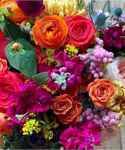 Designer's Choice and A gift TOO - A dense, color-packed mixed bouquet that reads like a celebration in bloom - perfect as a Mother's Day arrangement or for birthdays, congratulations, or a cheerful "just because" surprise. Hot pink roses and ranunculus-like blooms take center stage amid bright orange, purple, yellow, and white flowers, with green foliage and small clustered fillers adding lively texture; the overall look is playful and lush so the person you're sending it to will feel joy and noticed the moment it arrives.  Flowers are tightly layered for a full, rounded silhouette, the bouquet is arranged to read fresh and abundant from every angle.  Each order includes a simple floral scented wax candle in a clear glass jar - a understated extra that complements the flowers without competing. This combination makes a thoughtful gift for moms, friends, or anyone you want to celebrate; choose your size at checkout for a fuller or more petite presentation and enjoy fresh-cut flower care tips with your confirmation.