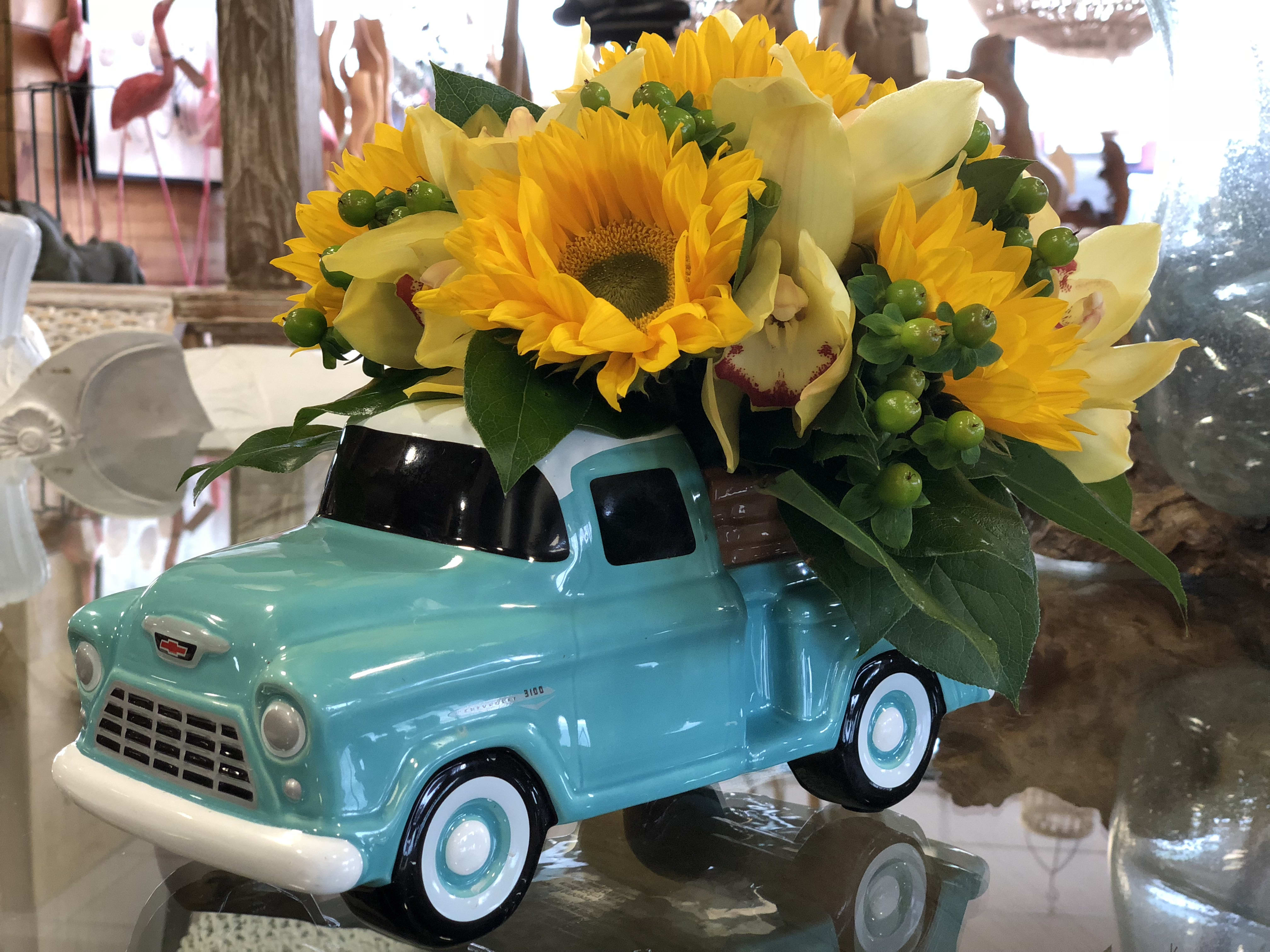Sunflowers and pale yellow orchids arranged in a turquoise truck planter