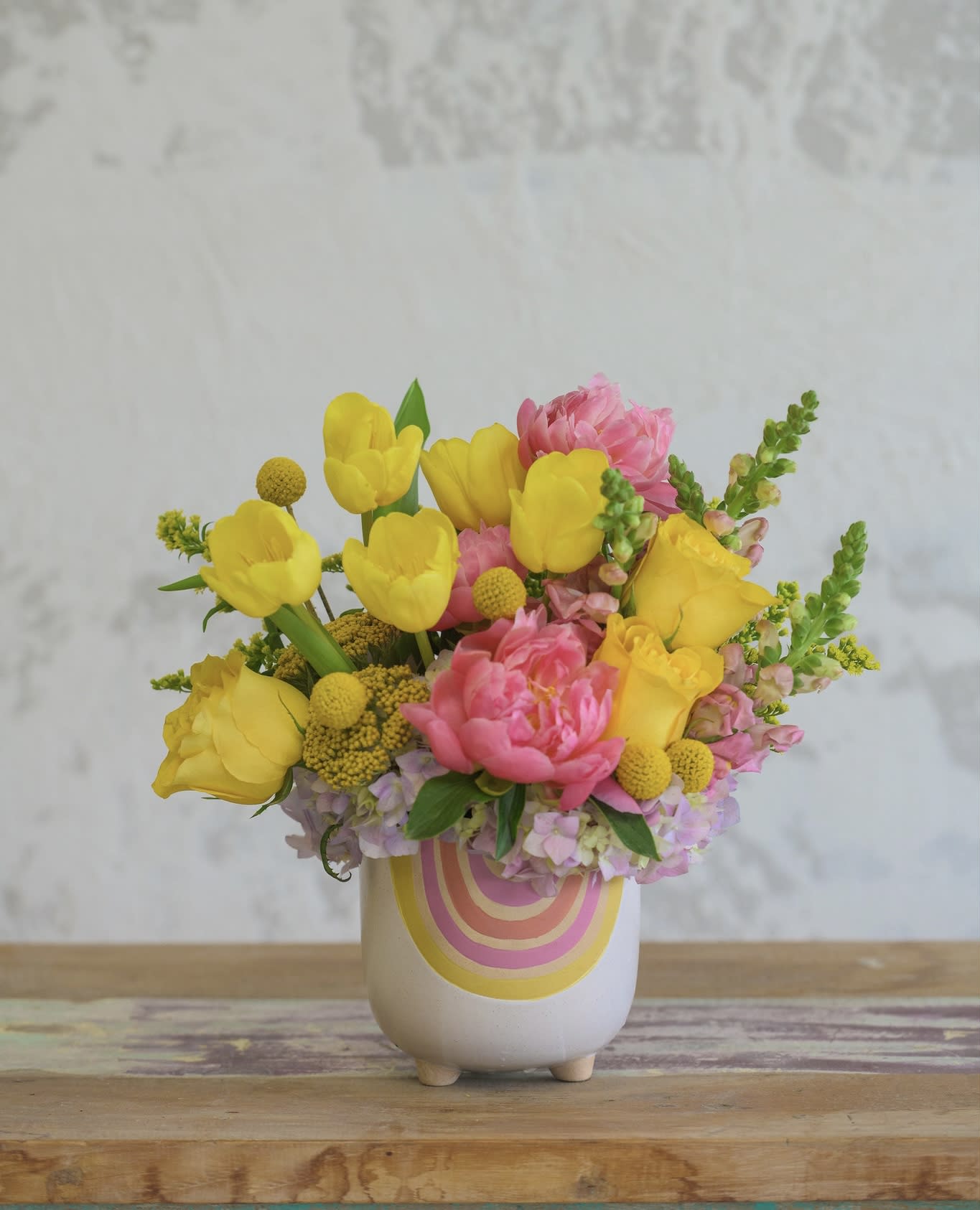 Yellow tulips and pink flowers in a white ceramic vase