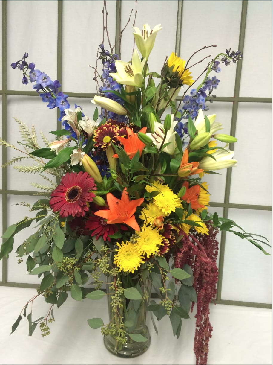 Tall mixed bouquet in a glass vase with lilies, gerberas, and blue flowers