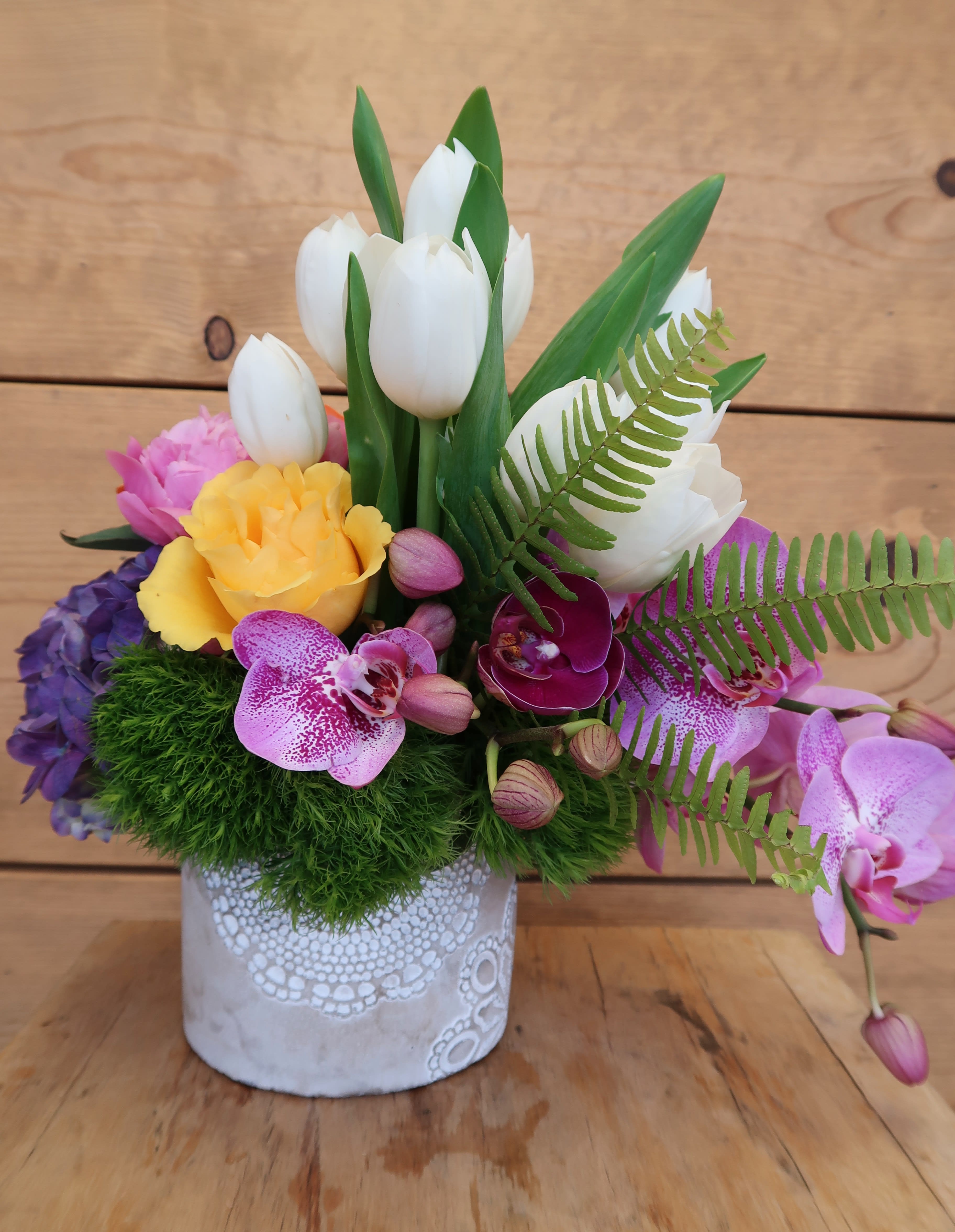 Colorful floral arrangement in a white decorative pot with tulips and orchids