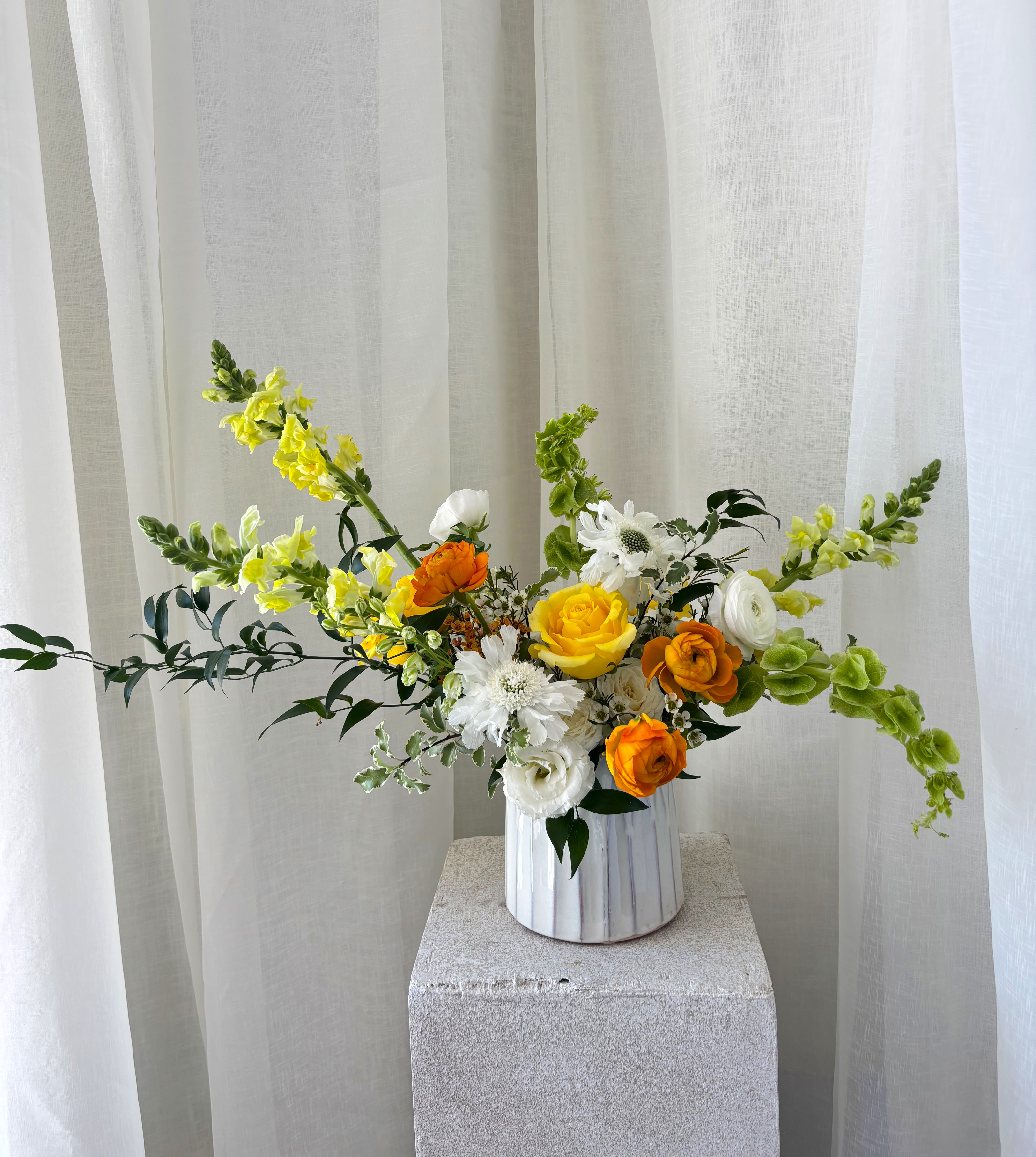 Yellow, white, and orange flowers in a white vase