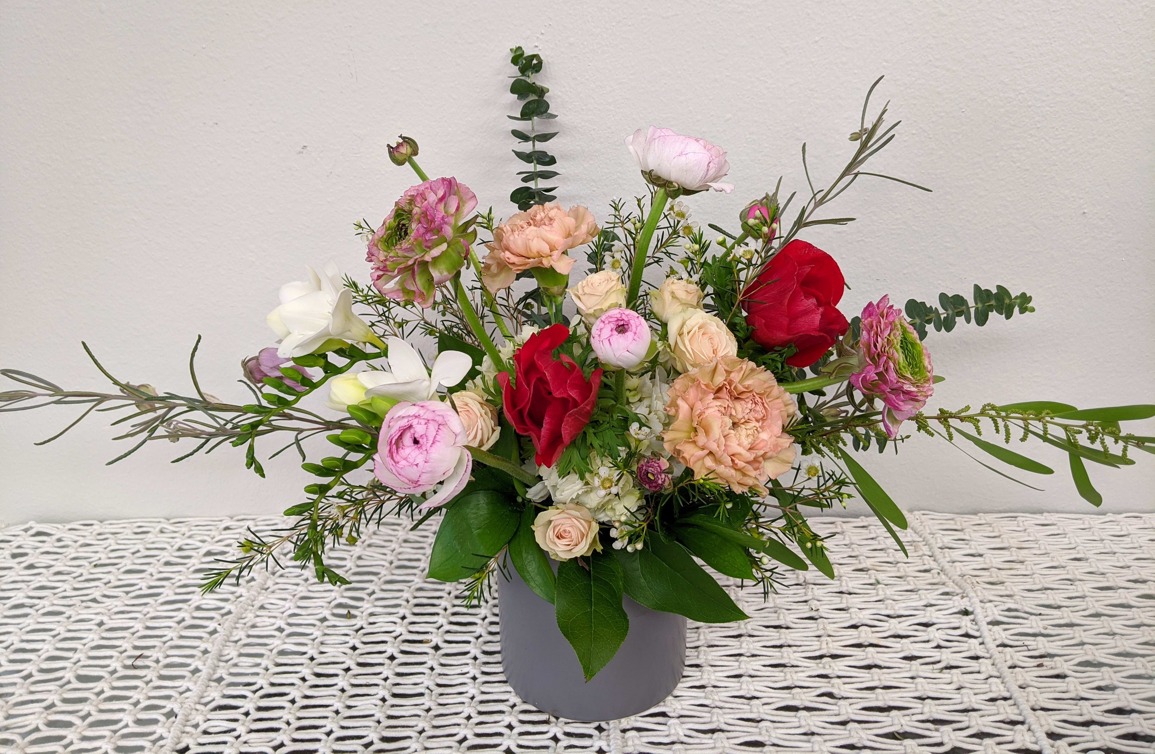 Mixed bouquet of pink, red, and white flowers in a gray vase