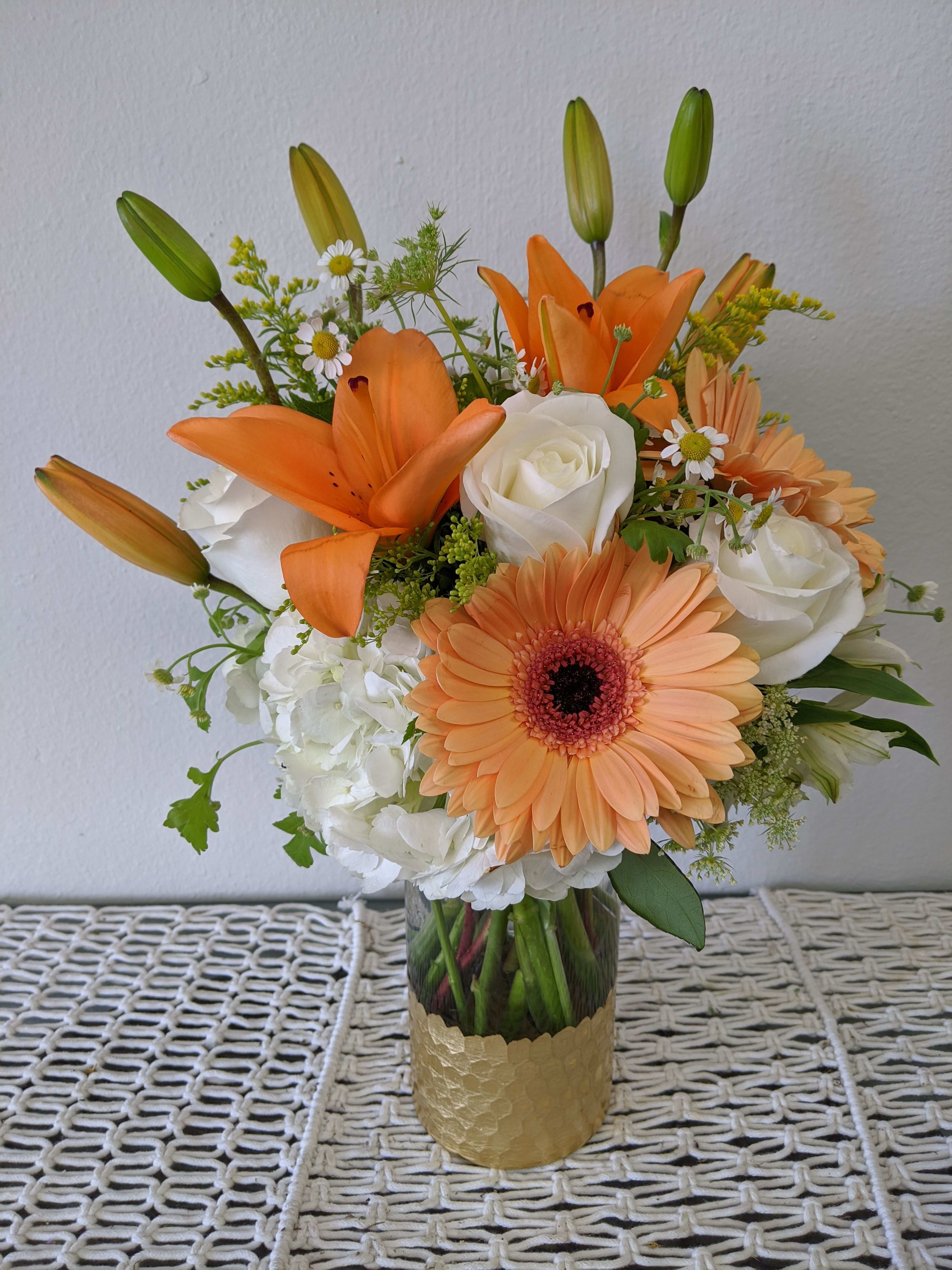 Orange lilies and peach gerbera daisies in a glass vase with white roses