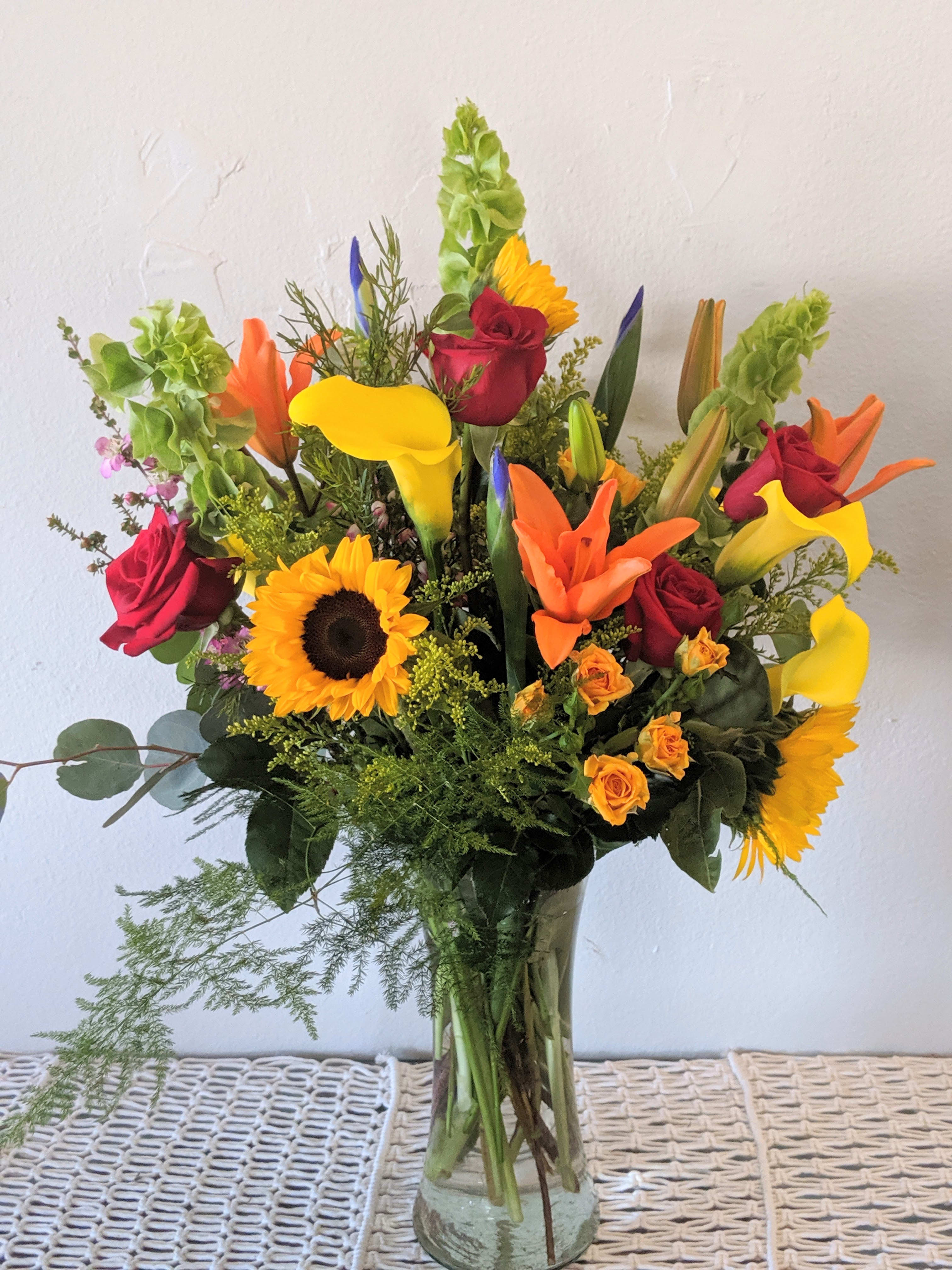 Mixed bouquet with sunflowers, roses, and calla lilies in a glass vase