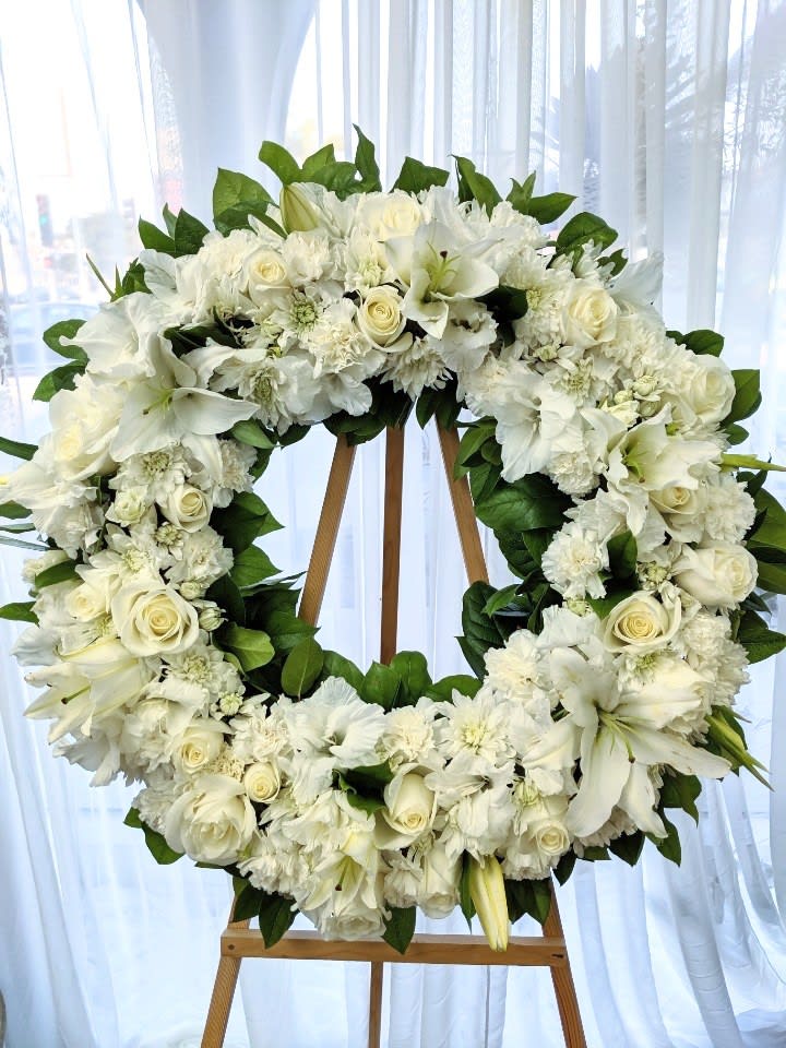 White floral wreath on a wooden easel with roses and lilies