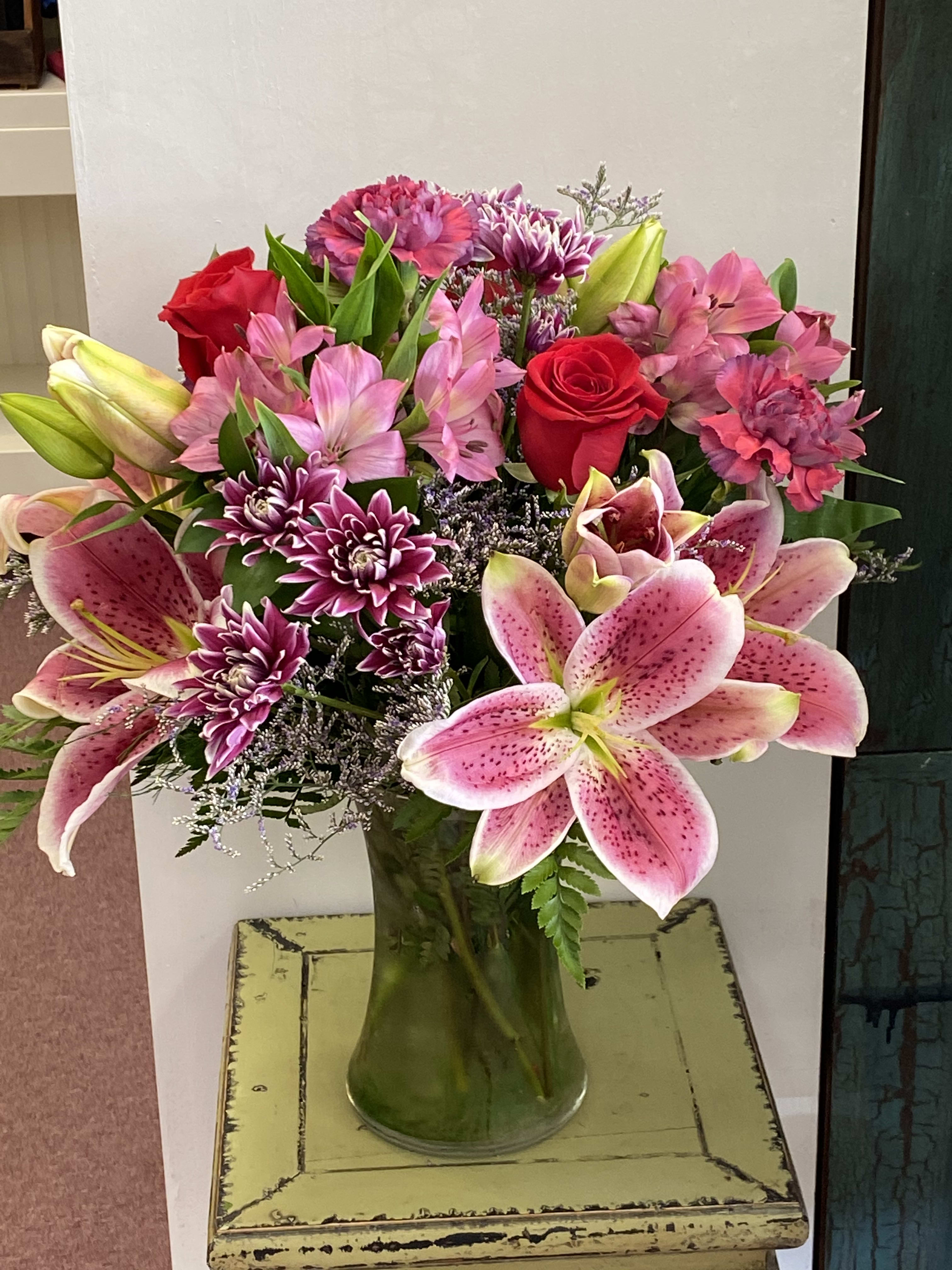 Mixed bouquet of pink lilies, red roses, and purple flowers in a glass vase