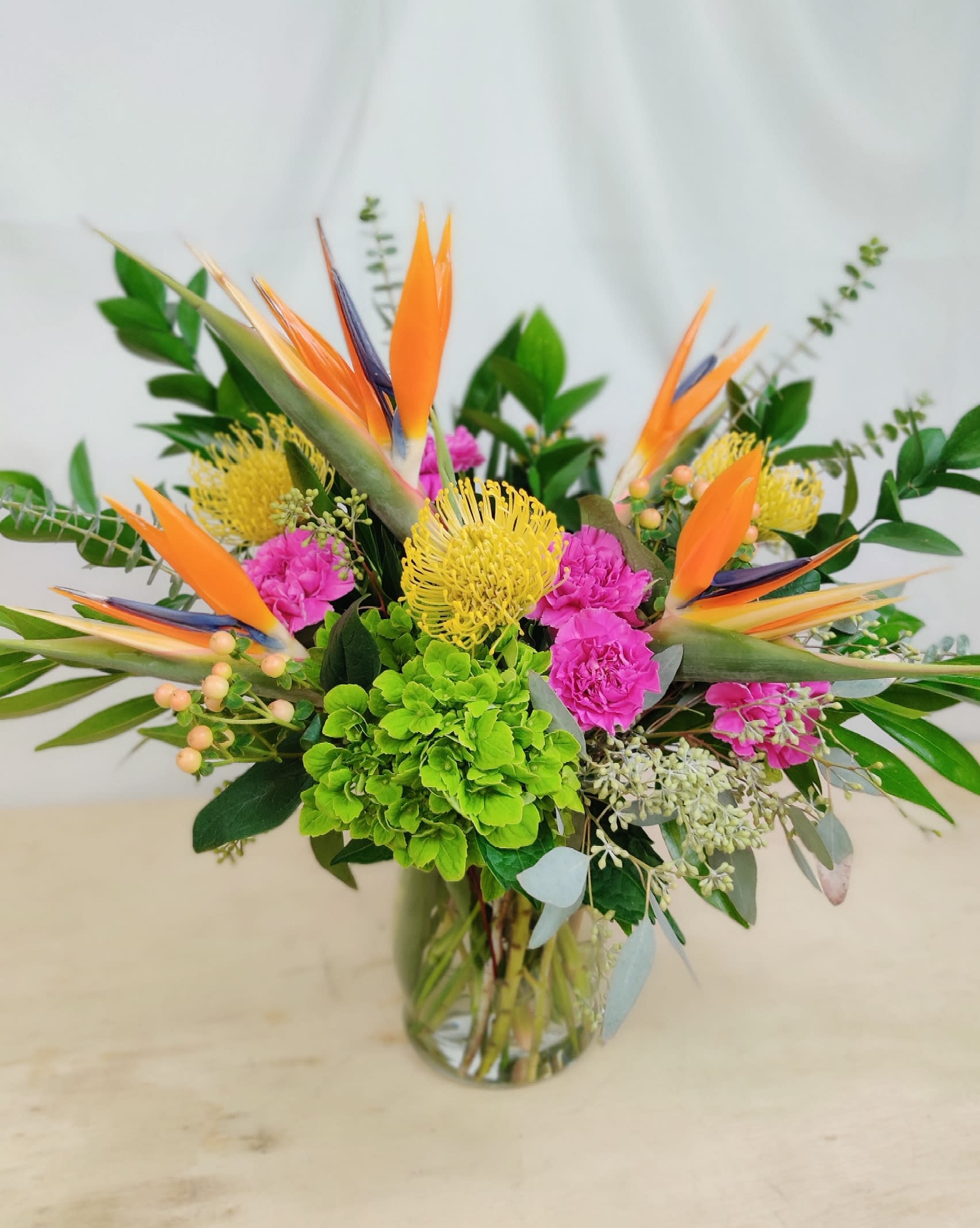 Tropical bouquet with orange bird-of-paradise and pink flowers in a glass vase