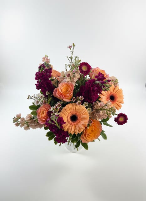 Mixed bouquet of orange roses and gerbera daisies in a clear vase