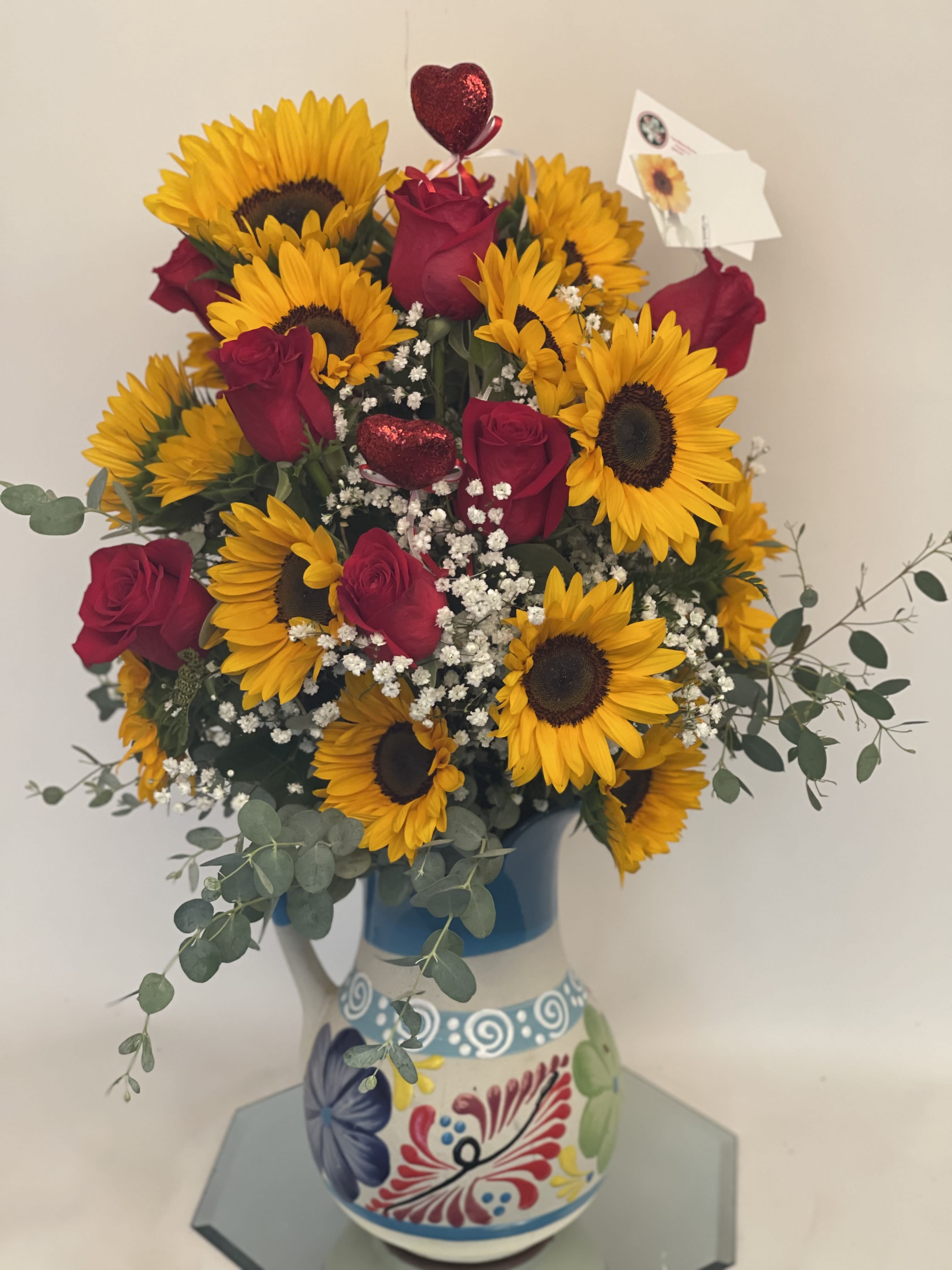 Bouquet of sunflowers and red roses in a painted ceramic pitcher