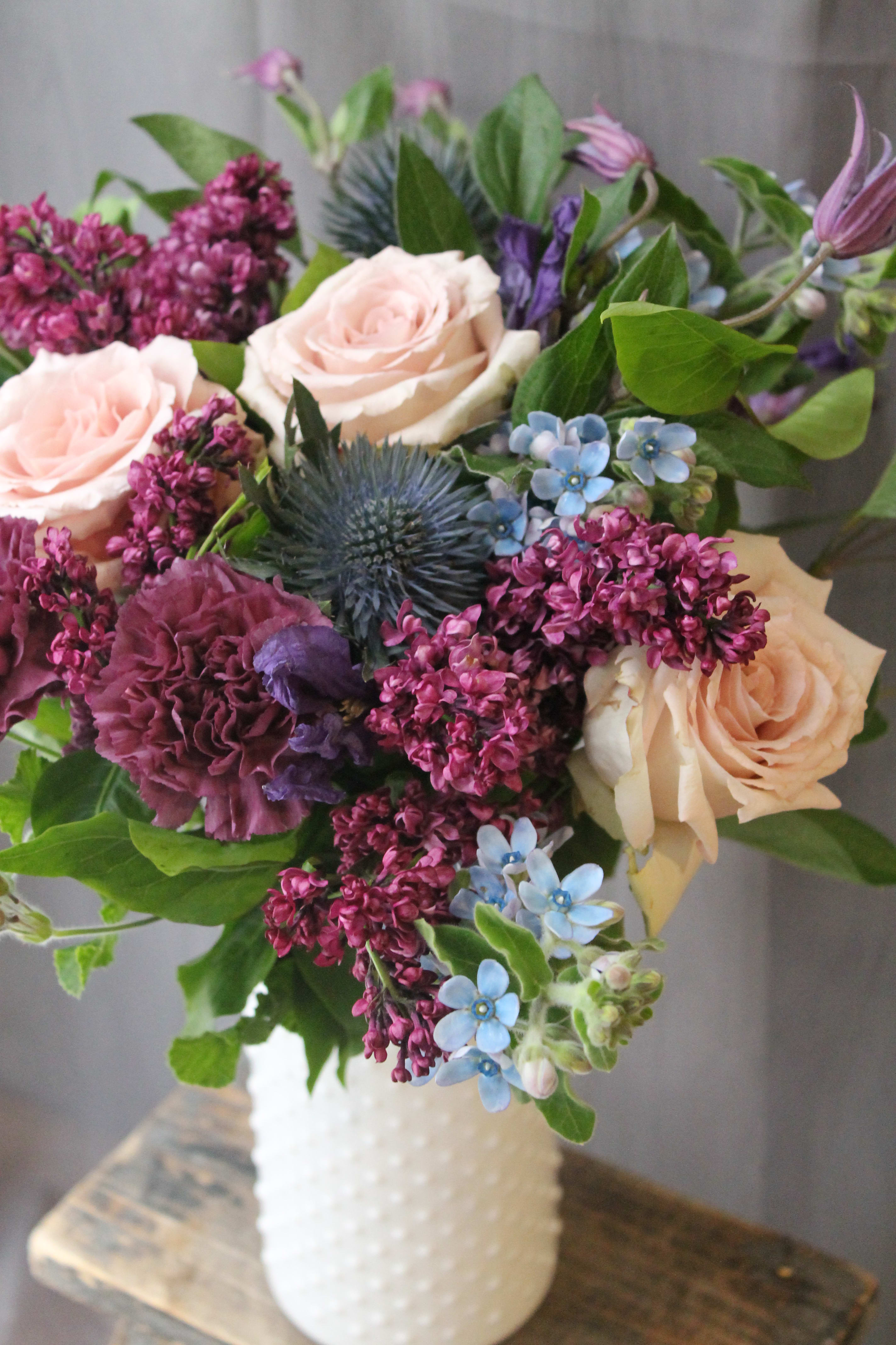 Vintage Fleur - Sweet lilacs, pink roses and touch of blue, arranged perfectly in a white vase.Gorgeous spring blooms. Perfect for Mother's Day!