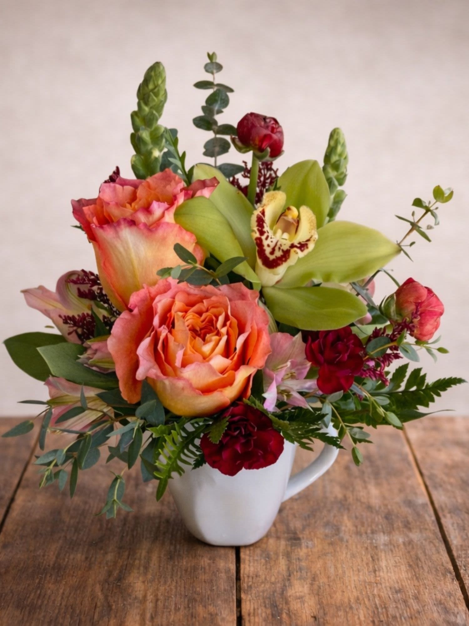 Mixed bouquet in a white mug with peach roses and green orchids