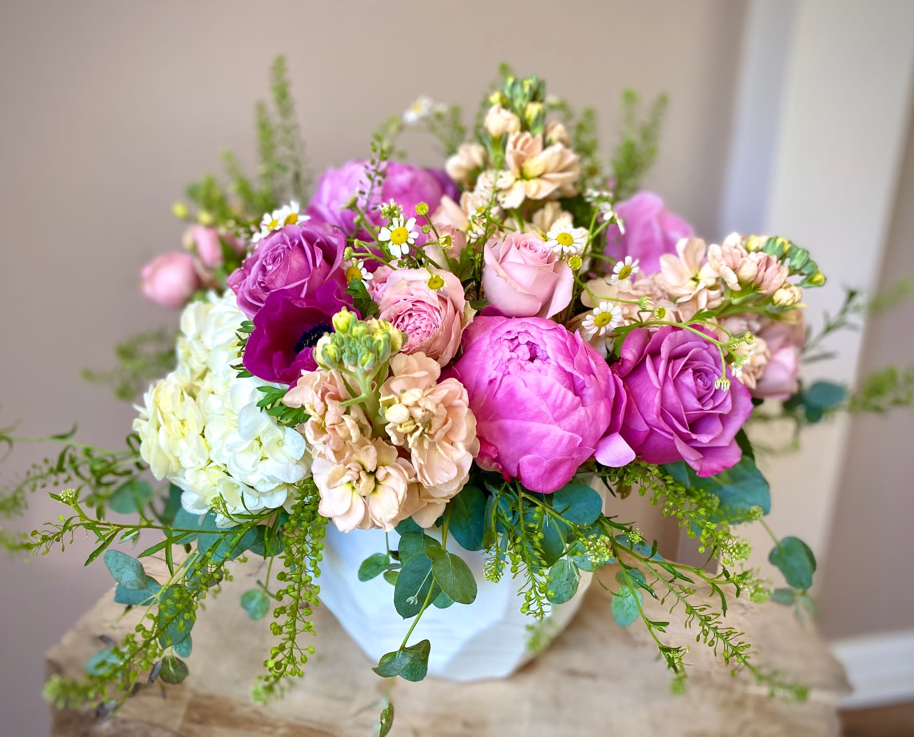 You're my happy place... - NOTE: Pictures show the DELUXE SIZE arrangement! This lush arrangement has the power to transmit you to your happy place! The fragrance and colors will surely brighten everyone's day! This arrangement is excellent for wishing your loved one a Happy Birthday or celebrating Anniversary, or Just Because... to let them know you're thinking of them and keeping them in your heart! It features a collection of seasonal Spring/Summer blooms in a variety of shades of pink and peach in a beautiful white ceramic vase.  The individual varieties of flowers will vary based on the freshest available blooms in this color scheme. Please note that peonies are not available all year round and will be substituted with other lush blooms when off-season. While the actual arrangement may not be exactly the same, it will have a similar value, look and feel and will feature the freshest seasonal blooms, greenery, and other elements available that day.   The arrangement may include the following: - roses - stock - hydrangea - anemone - spray roses - peonies, when in season - greenery  * The flowers will come arranged in a beautiful ceramic vase (shape and color may vary upon availability). 