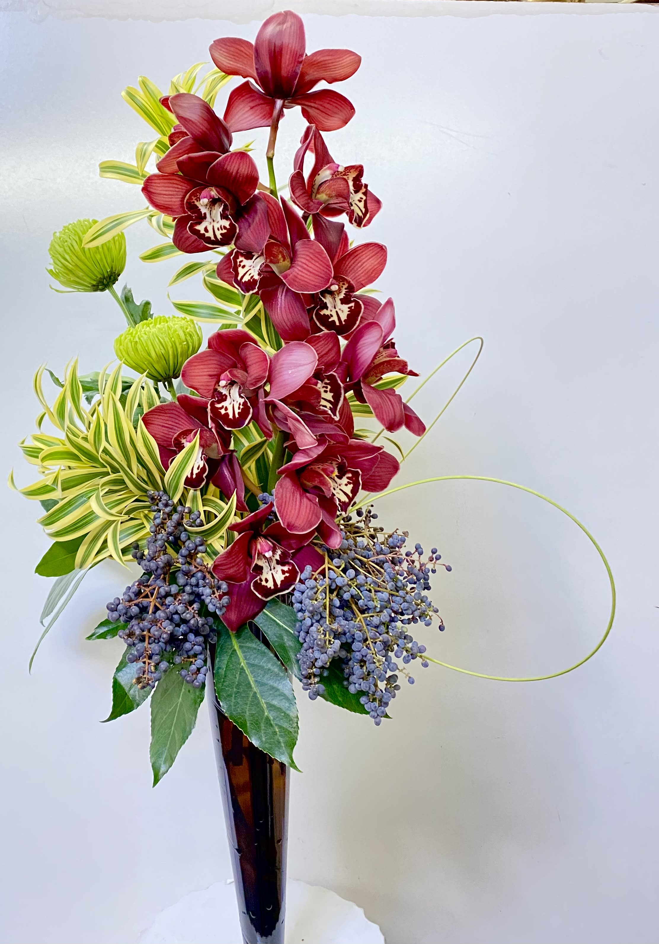 Tall arrangement of red orchids in a dark vase with green accents