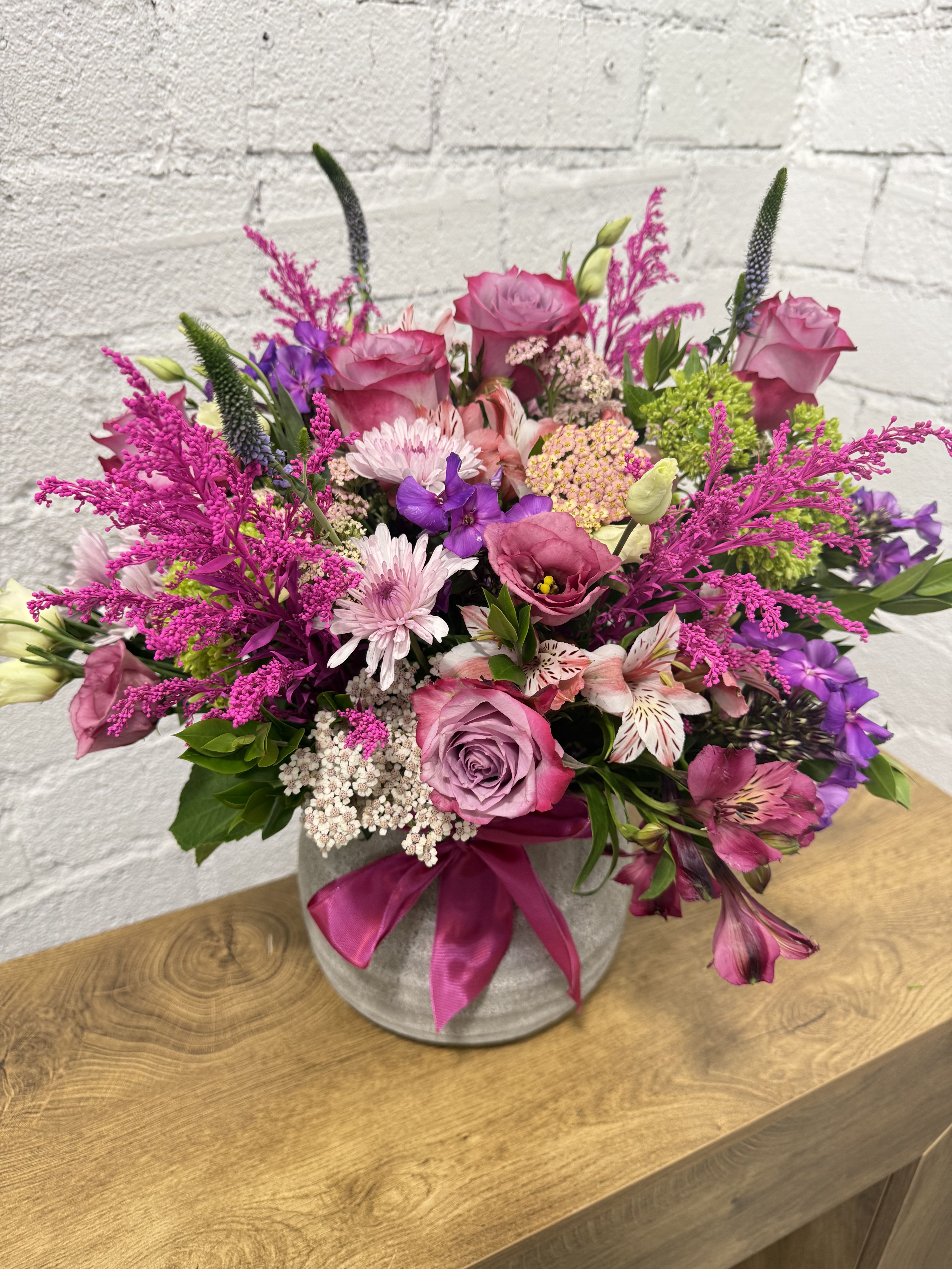 Pink and purple mixed bouquet in a gray vase with a satin ribbon
