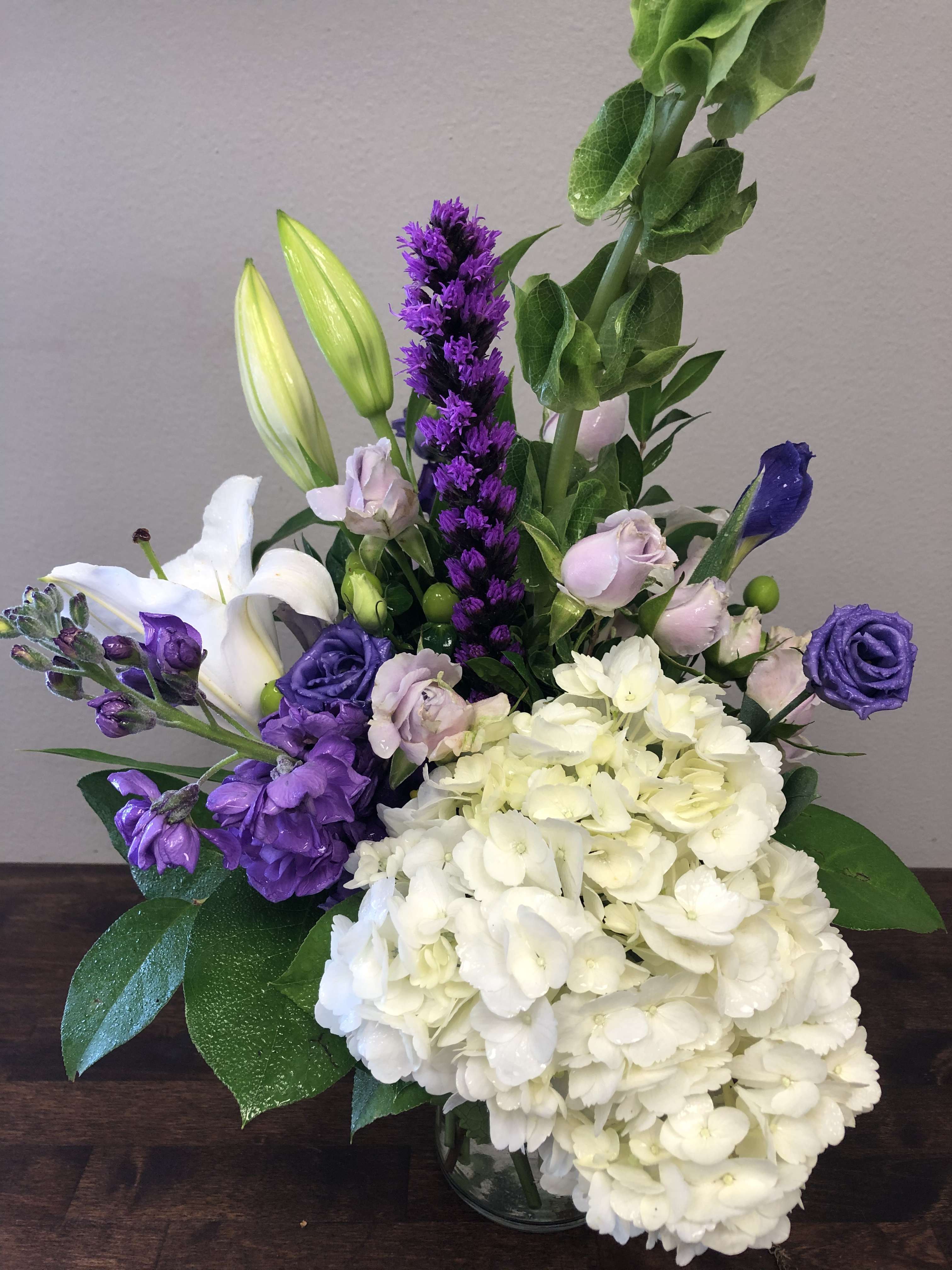 Purple and white floral arrangement with lilies, roses, and hydrangeas in a glass vase