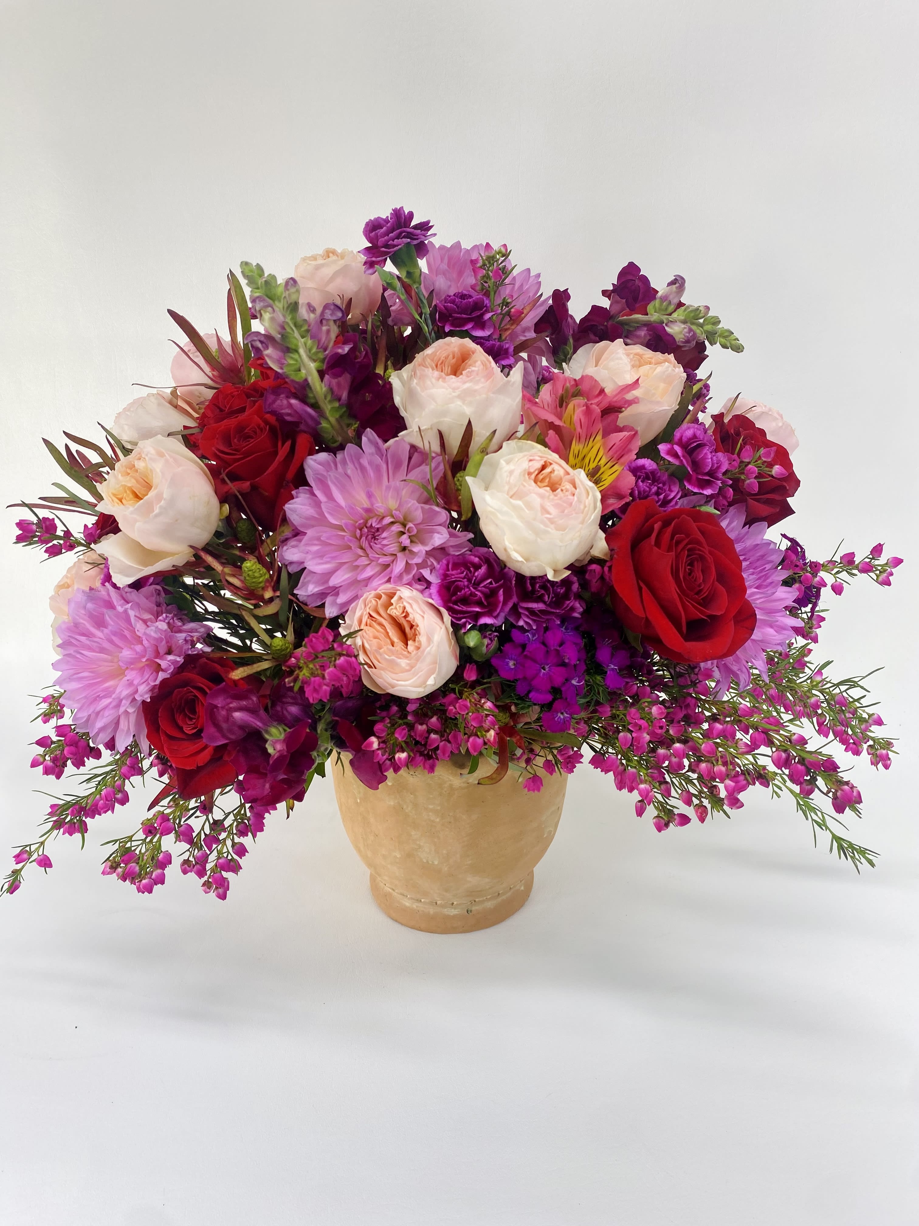 Mixed bouquet of red, pink, and peach flowers in a tan vase