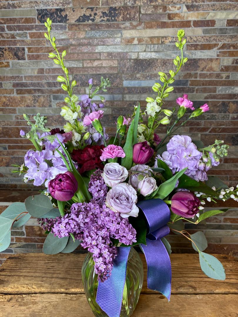 Purple and lavender bouquet in a glass vase with a ribbon