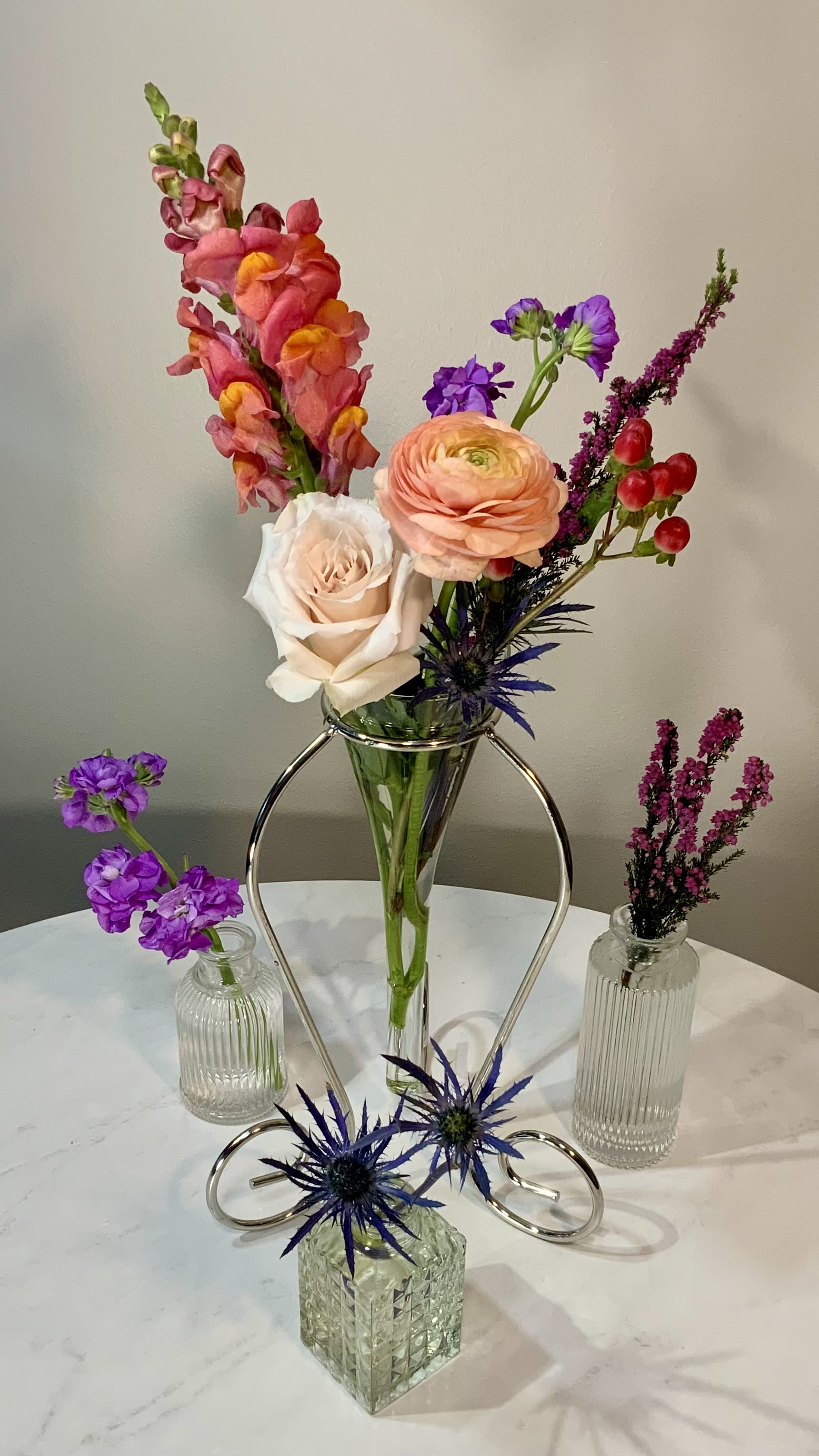 Mixed flowers arranged in a clear vase with small accent vases on a table