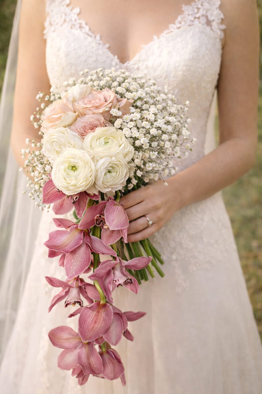 Bride holding a bouquet of white and blush flowers with trailing pink orchids