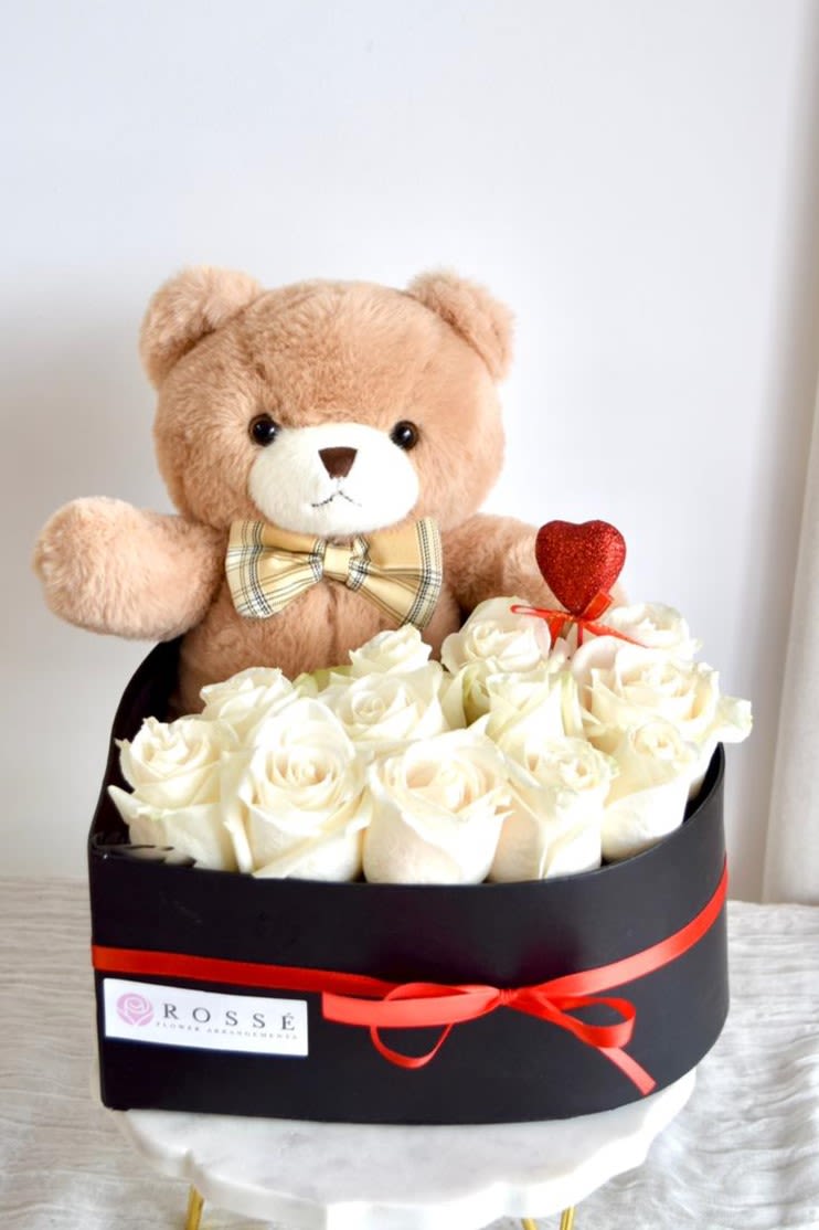 Teddy bear in a box with white roses and a red heart pick