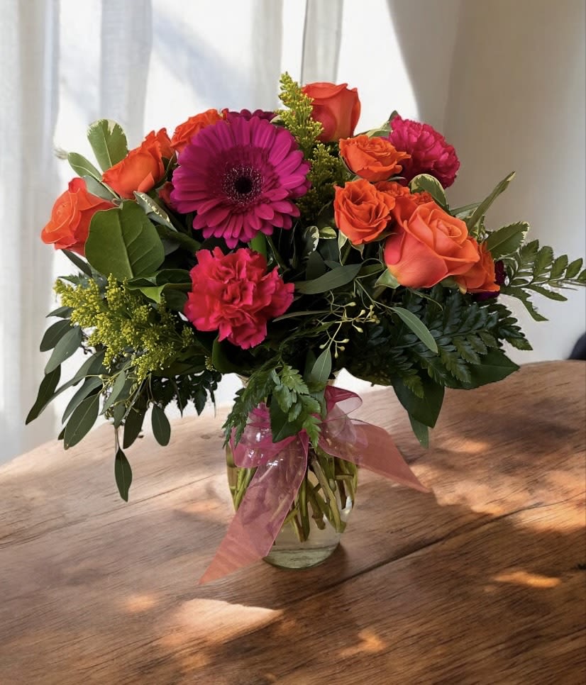 Bouquet of orange roses, pink gerbera daisies, and carnations in a glass vase