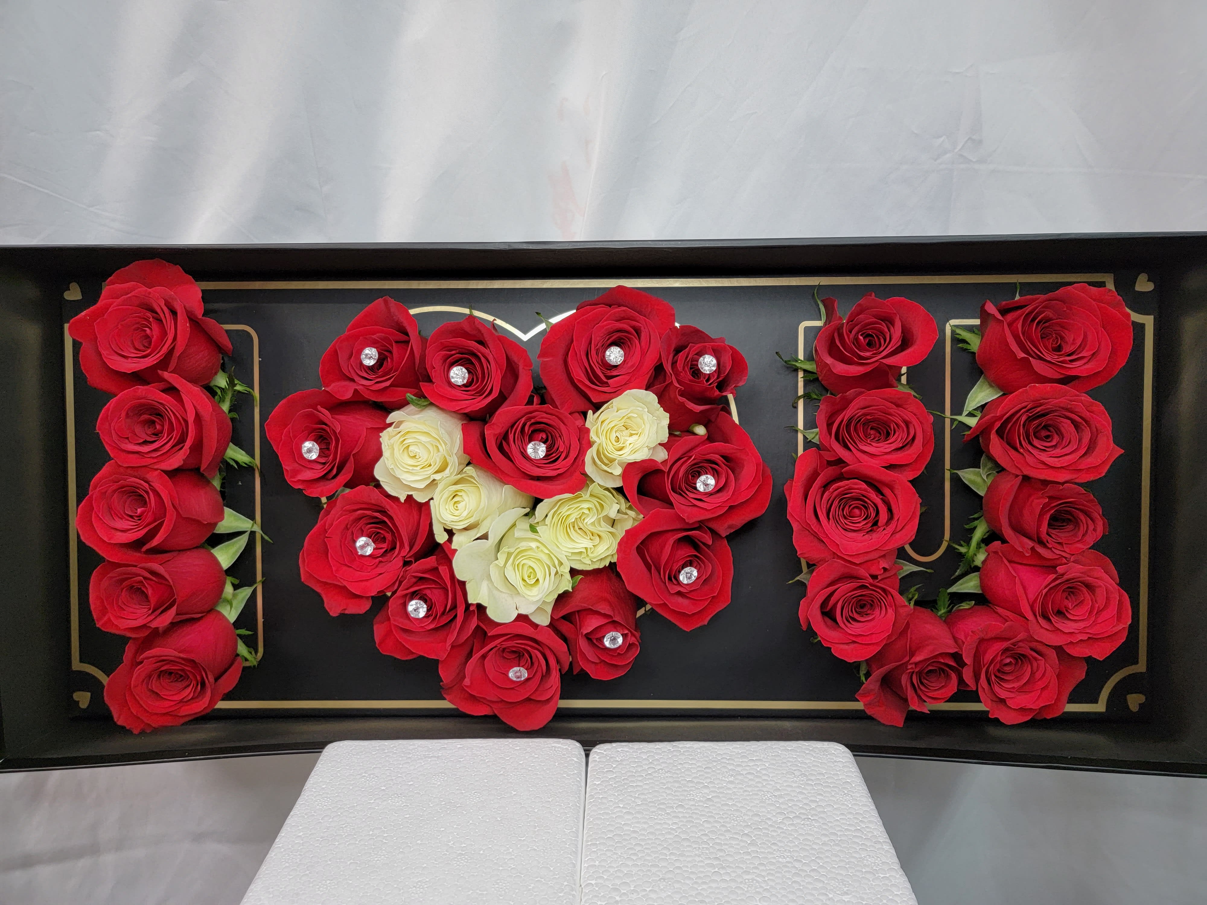 Red and white roses arranged in a black display box spelling "MOM"