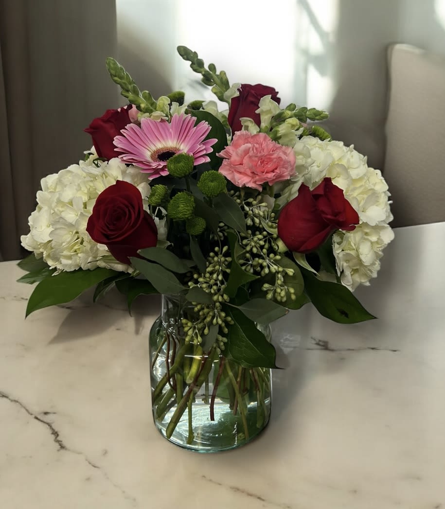 Bouquet of red roses, pink gerbera daisy, and white hydrangeas in a glass vase