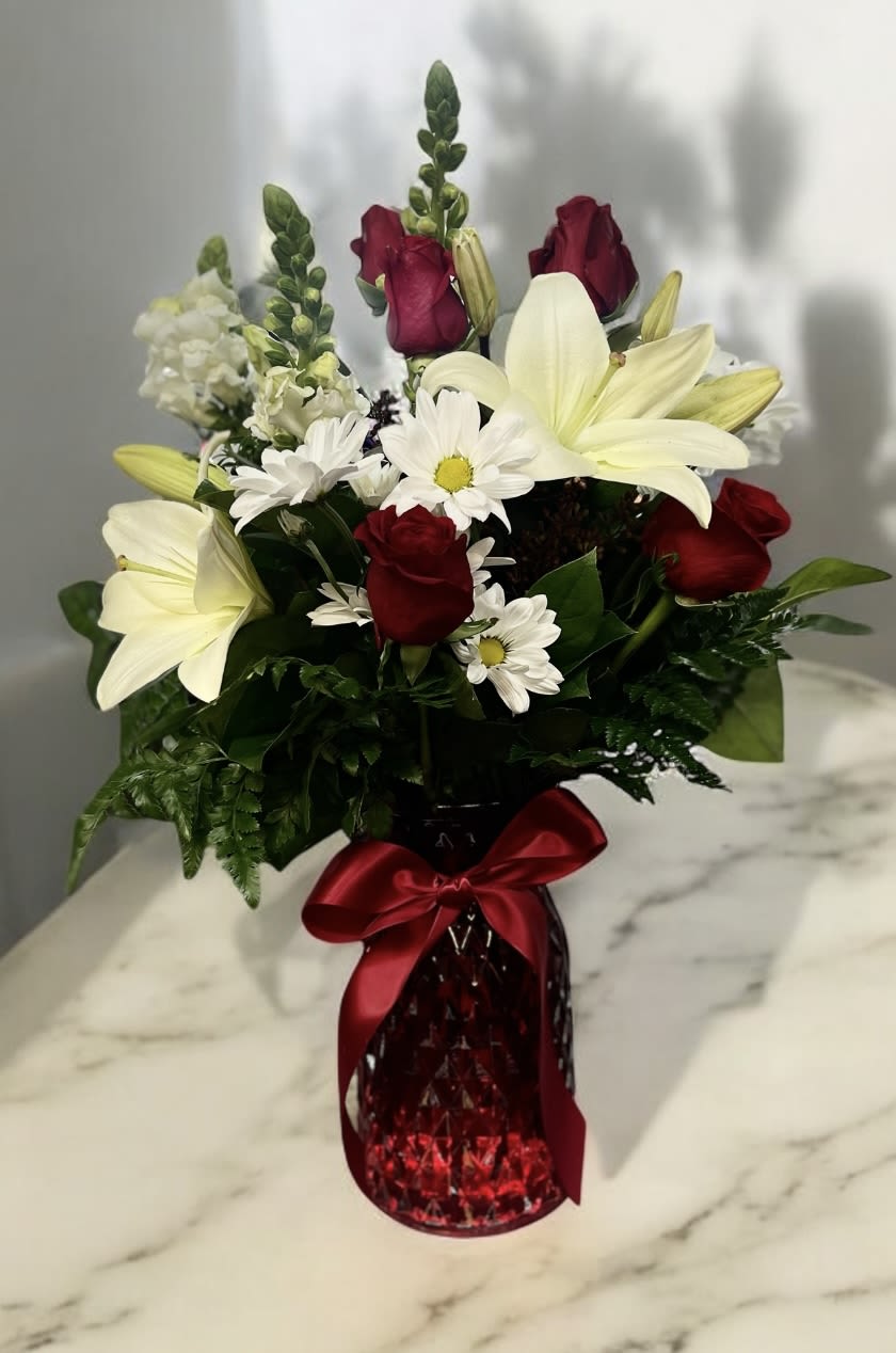 Red roses and white lilies in a red glass vase with a satin bow