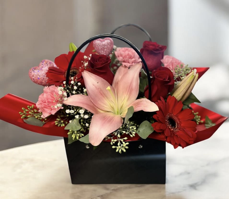 Red and pink flower arrangement in a black handled gift box