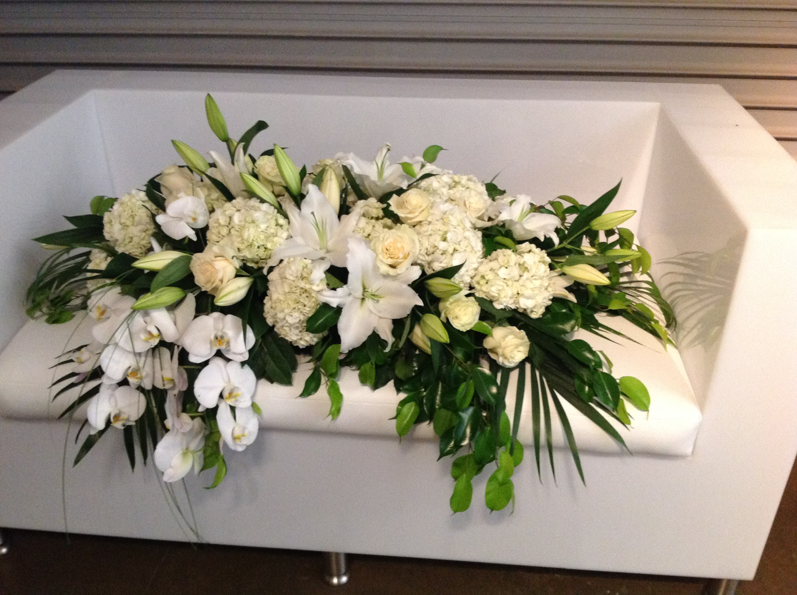 White floral arrangement with lilies, roses, and orchids on a white couch