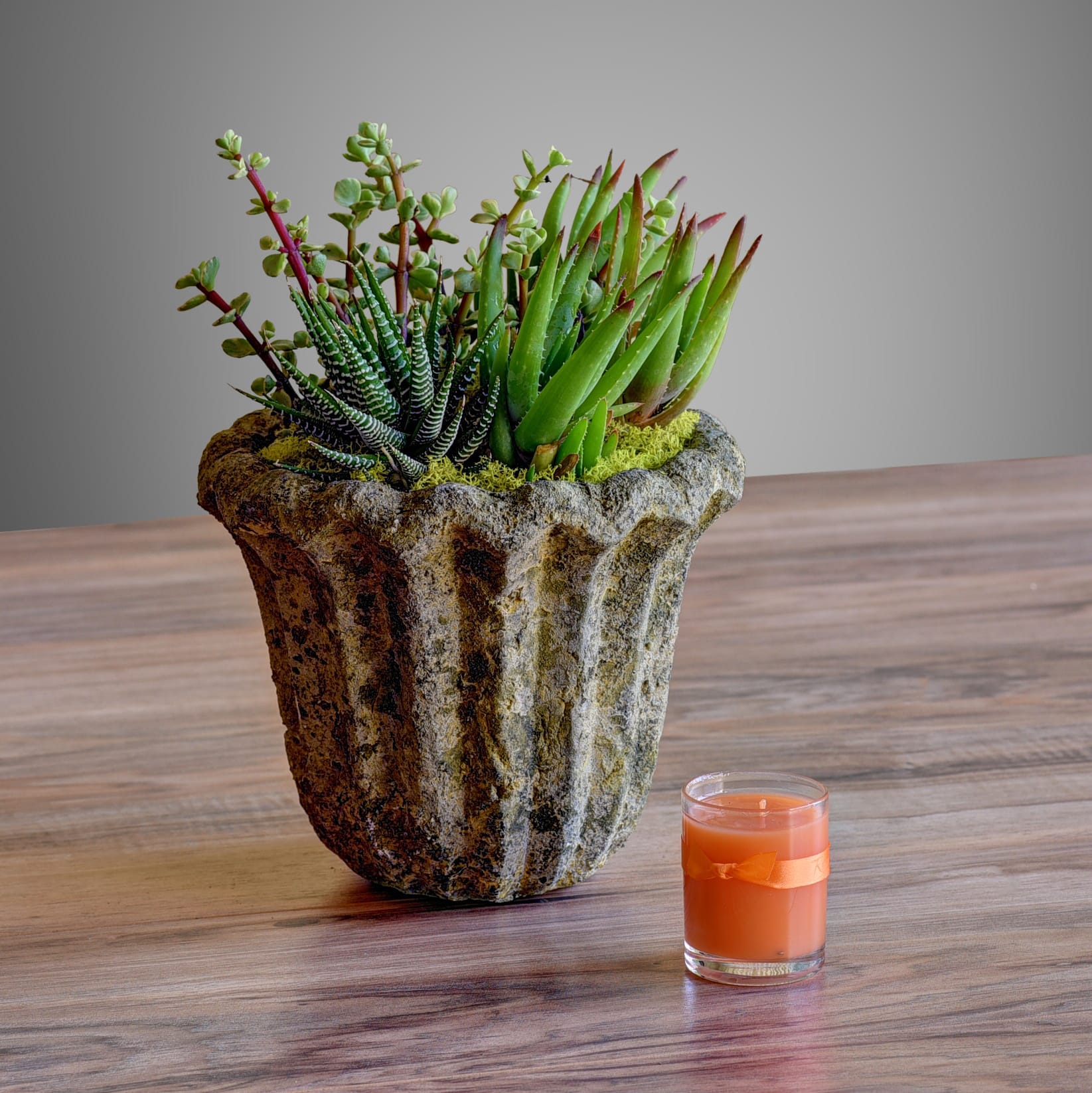 Succulent arrangement in a textured stone planter beside an orange candle