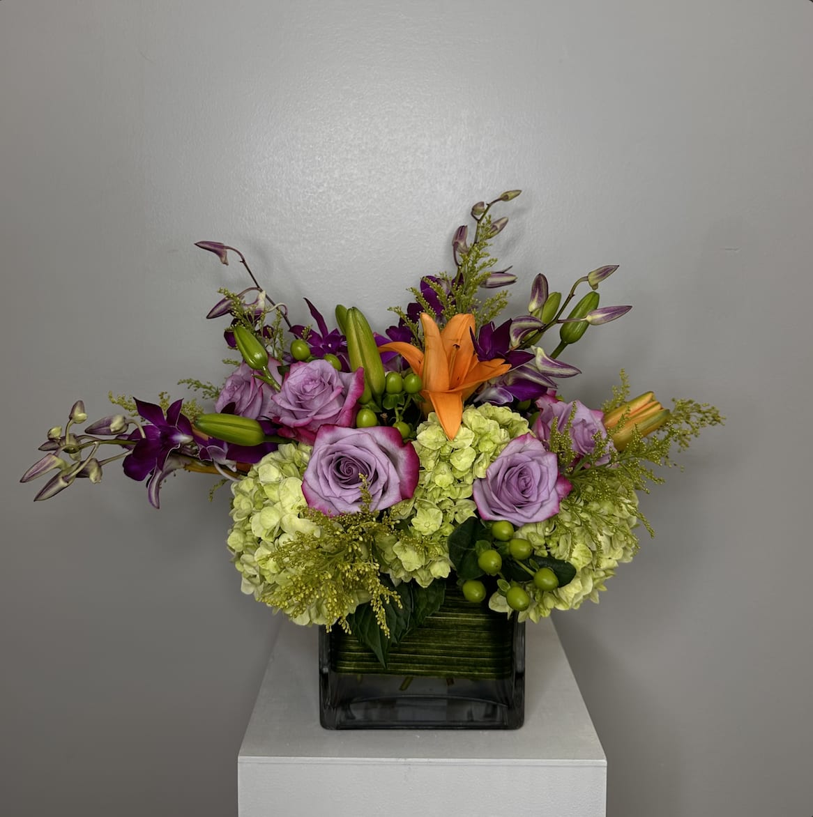 Lavender roses and orange lilies in a square glass vase