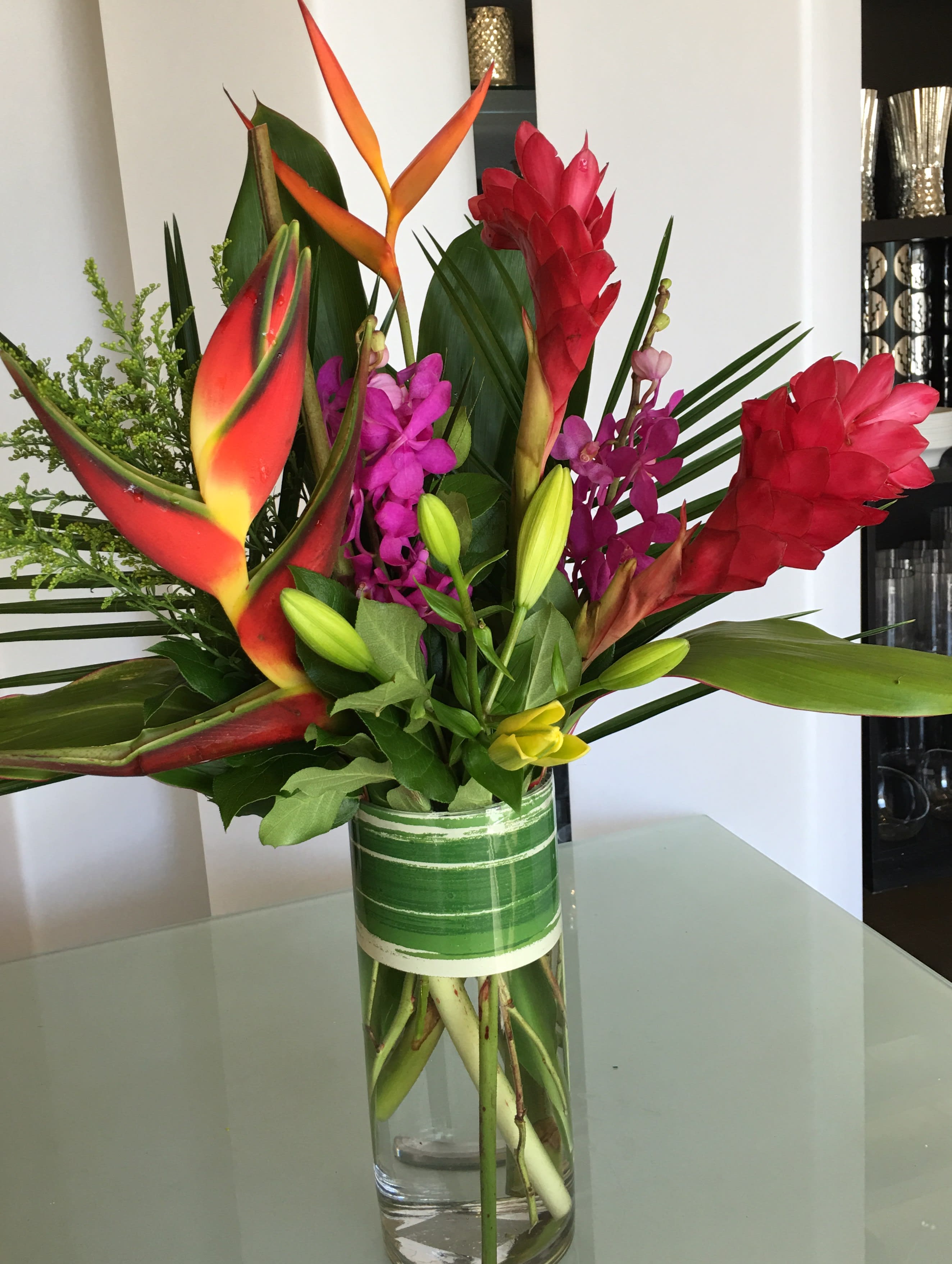 Tropical bouquet with red heliconia and purple orchids in a glass vase